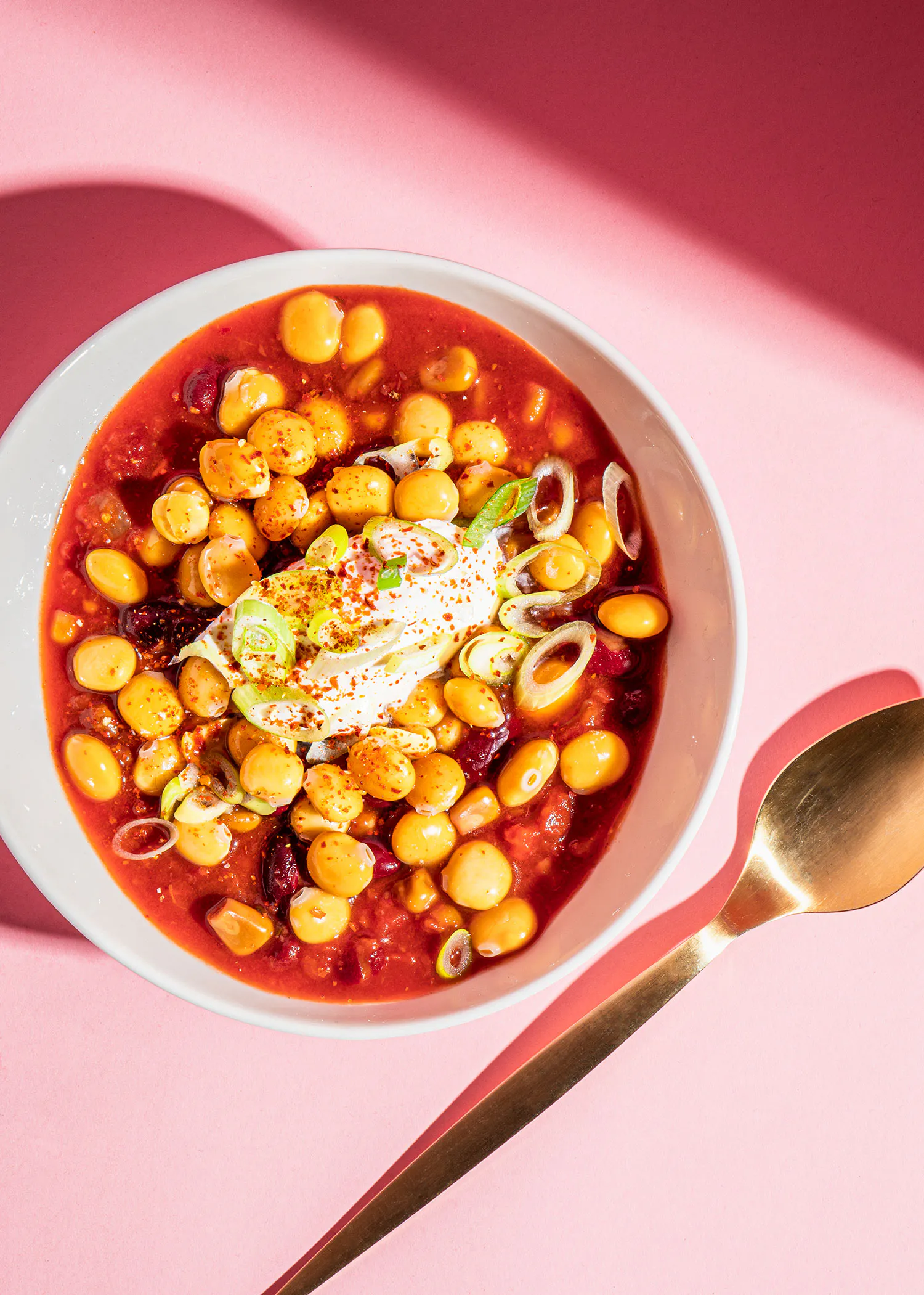 un bol de soupe avec des haricots et de la crème sure sur une table rose