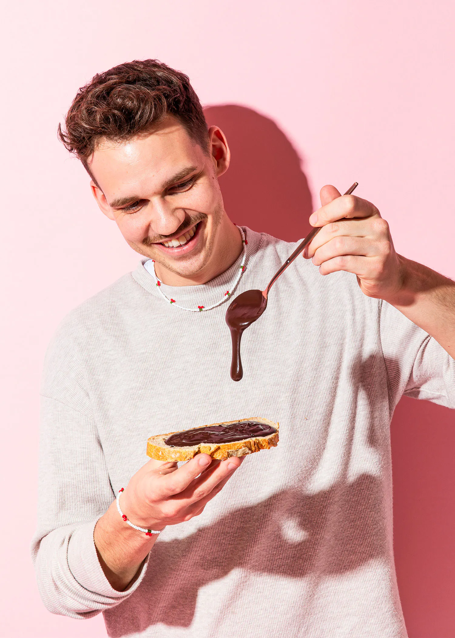 un homme sourit en versant du chocolat sur un morceau de pain