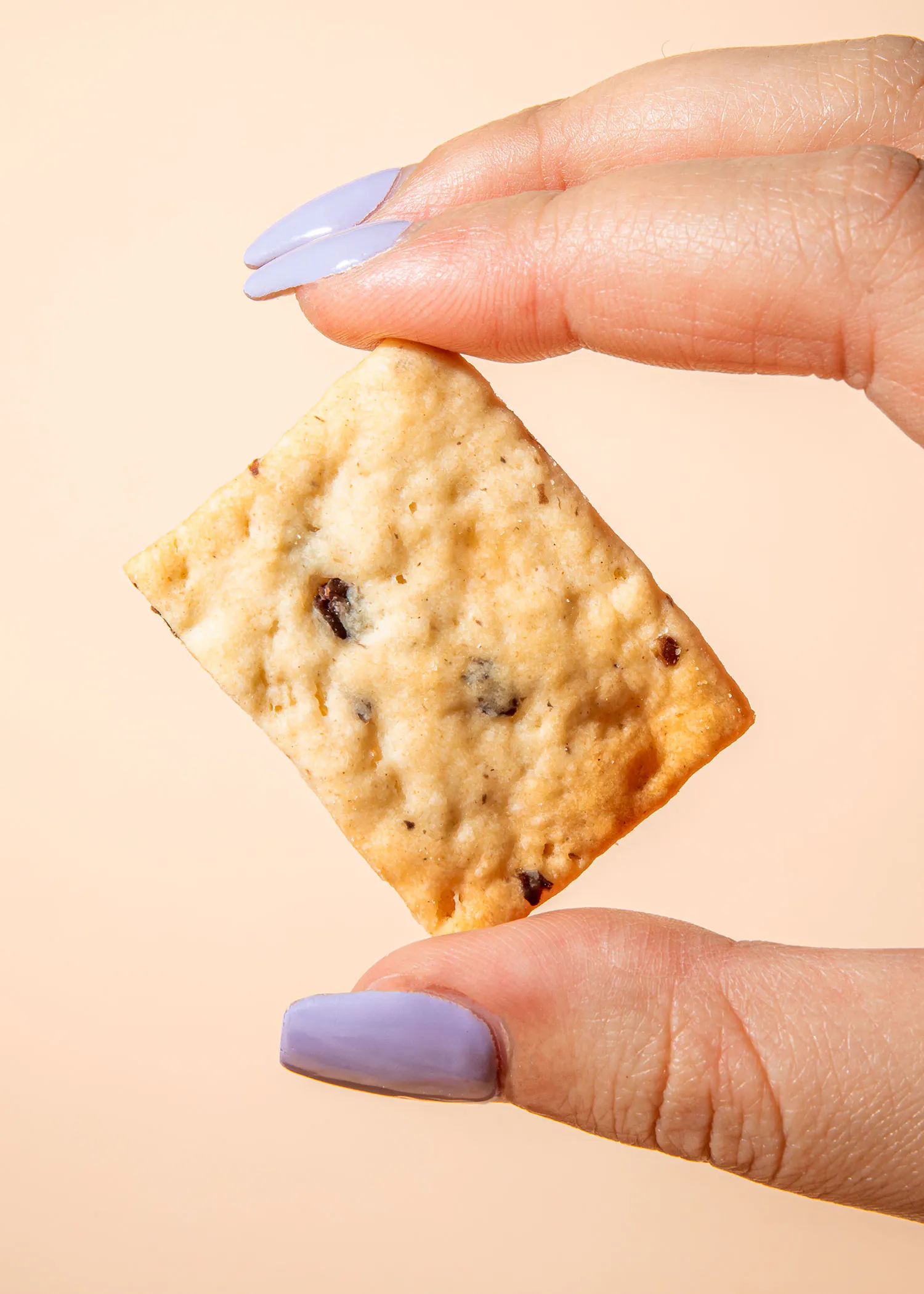 eine Frau mit lila Nägeln hält ein Cracker in der Hand