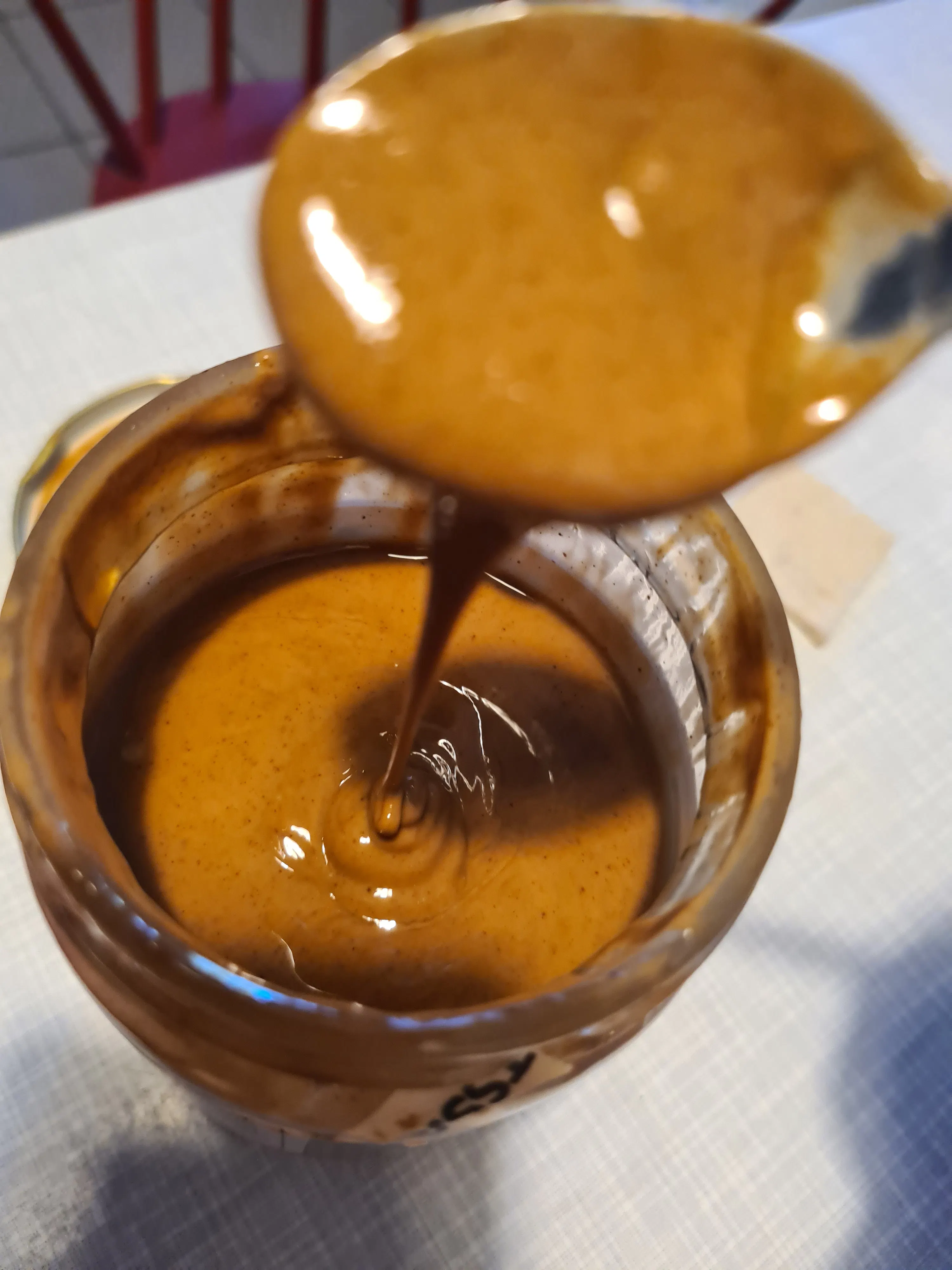 une cuillère verse du beurre de cacahuète dans un bocal