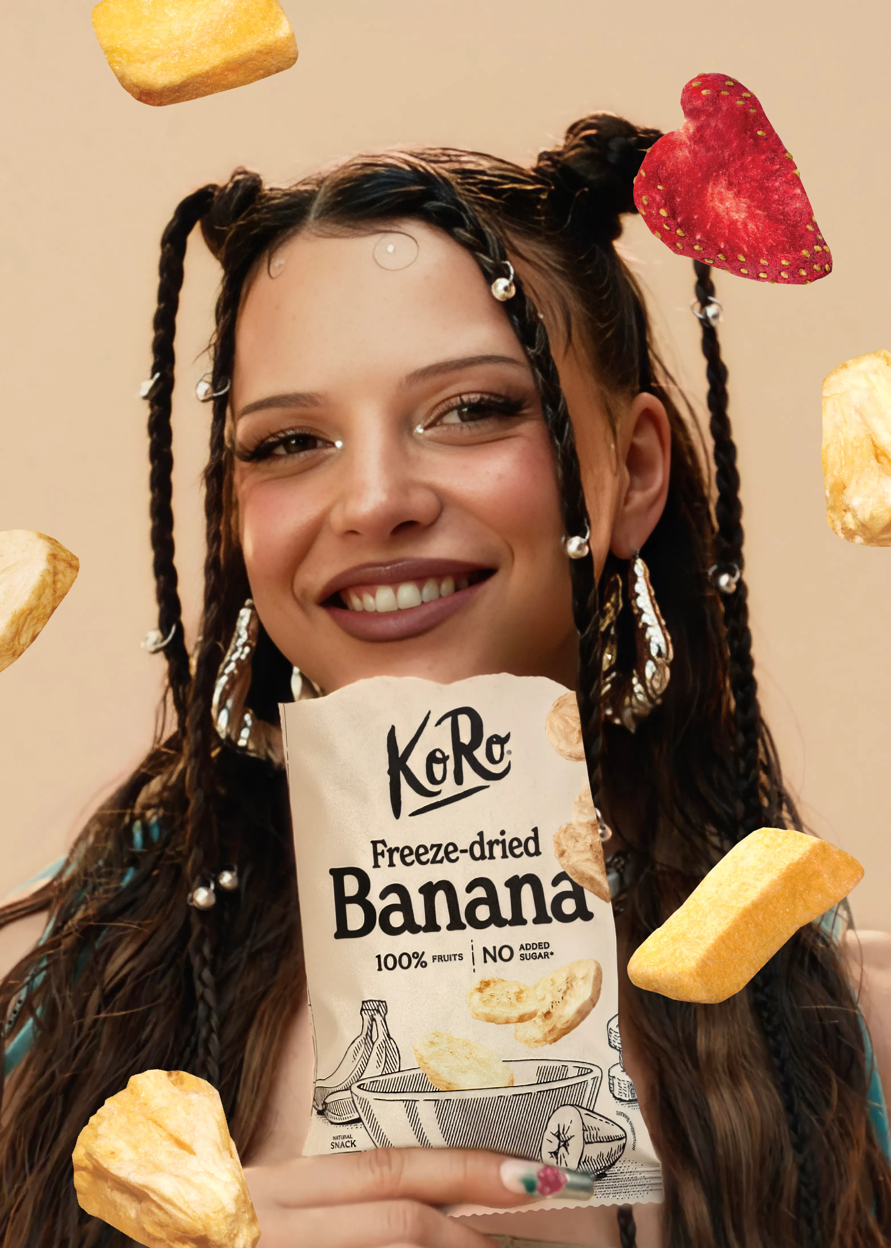 une jeune femme souriante tient un sachet de bananes lyophilisées koro entourée de morceaux de fruits flottants.