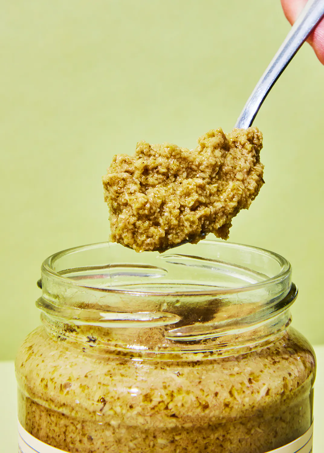 une personne tient une cuillère remplie de sauce à l' intérieur d' un bocal