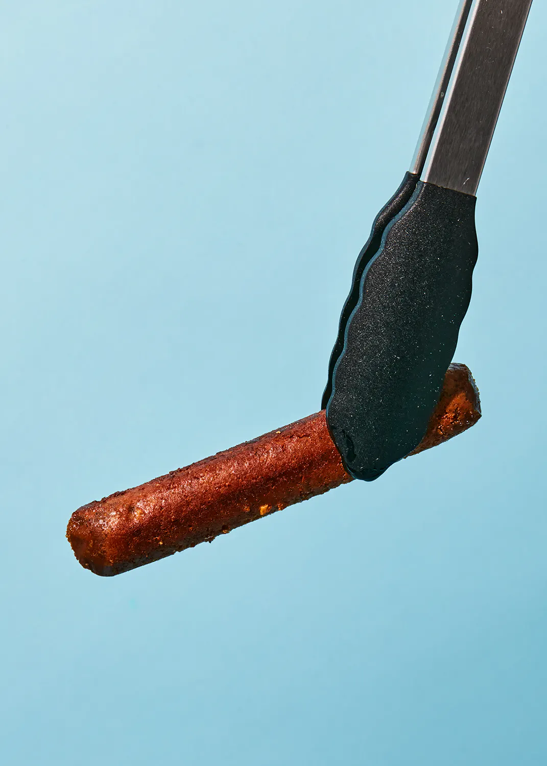 une paire de pinces tient une saucisse sur un fond bleu