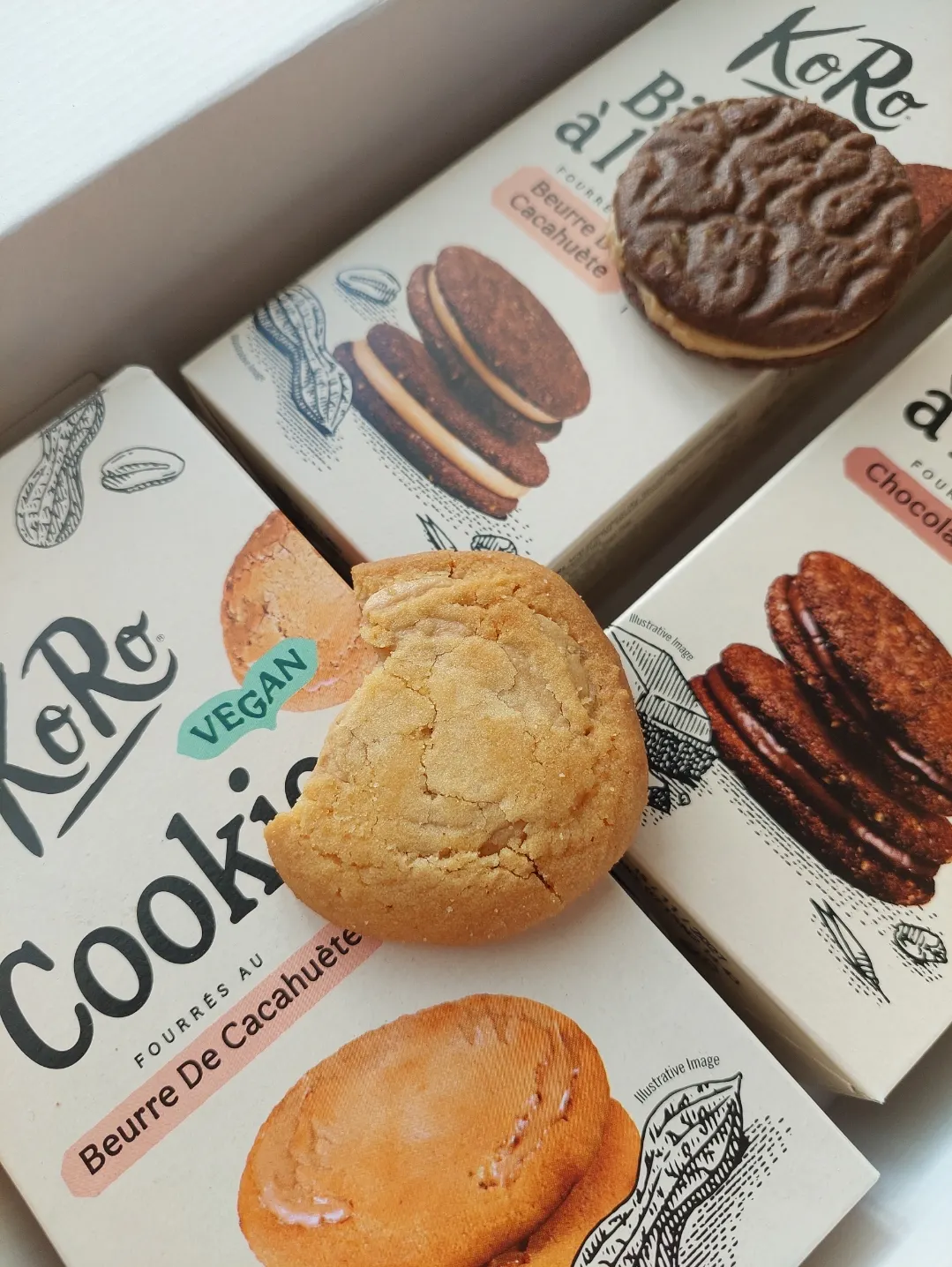 una selezione di confezioni di biscotti koro con diversi gusti, tra cui burro di arachidi e cioccolato, disposte con alcuni biscotti appoggiati sopra.