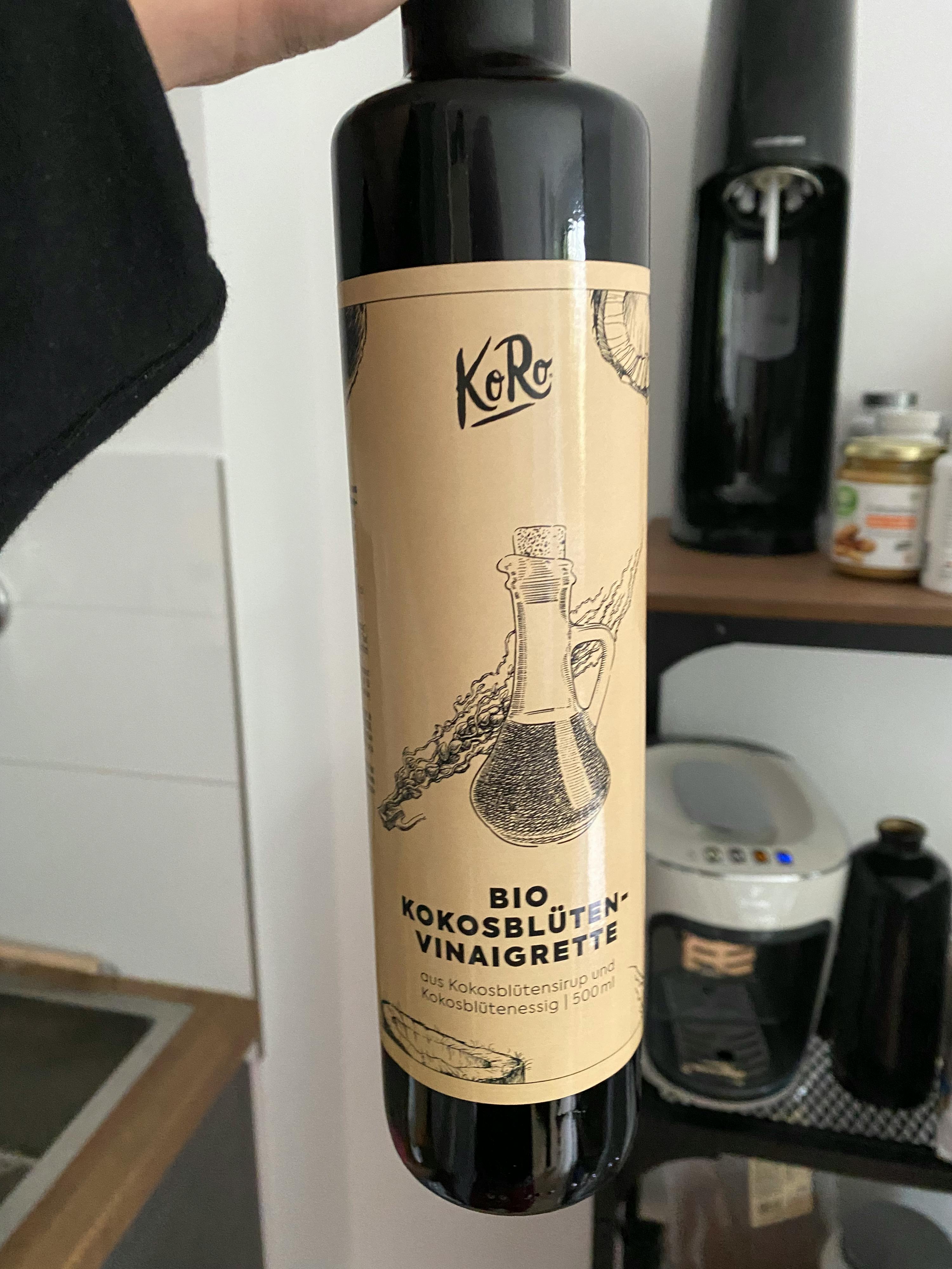 una persona tiene in mano una bottiglia di bio kokosblumen vinaigrette