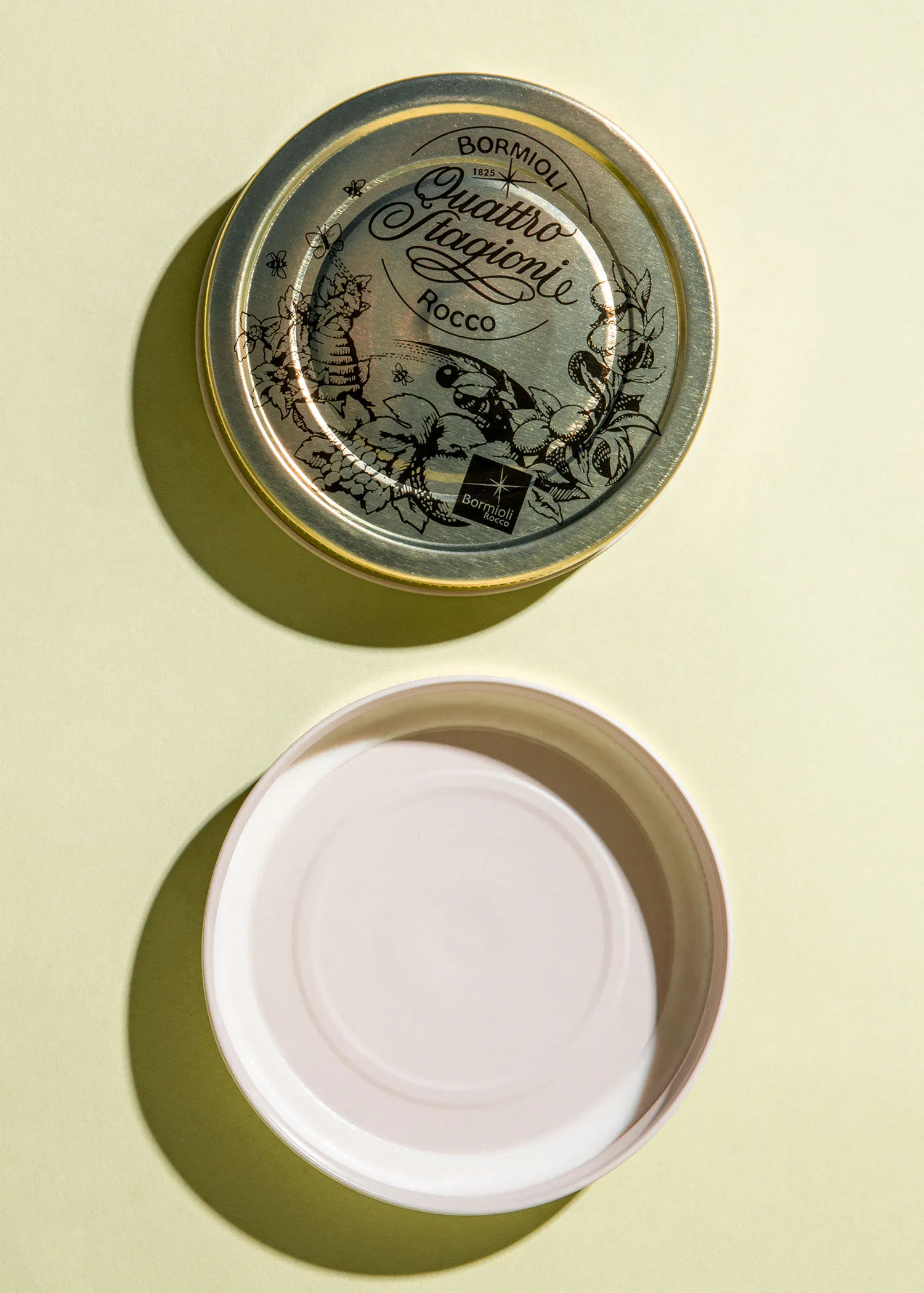 ein silberner Deckel mit der Aufschrift quattro stagioni rocco neben einem weißen Teller