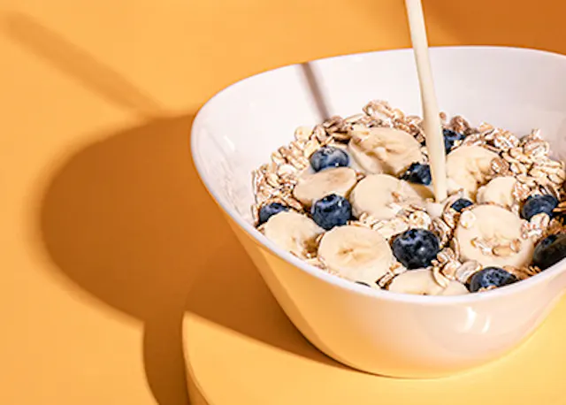 Milch wird in eine Schüssel Haferflocken mit Bananen und Blaubeeren gegossen