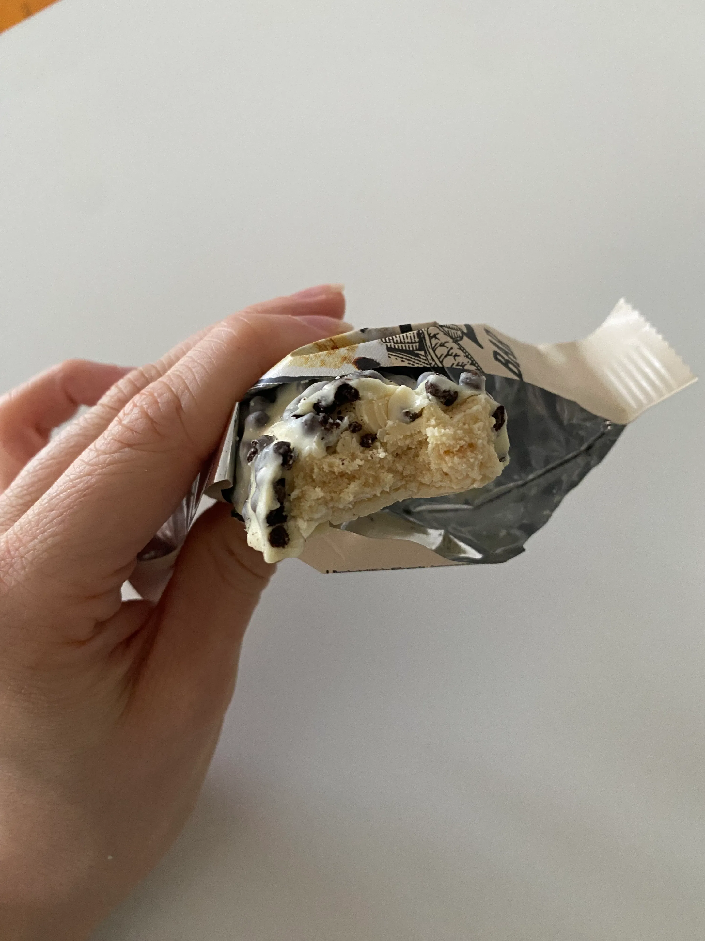 una mano tiene una barretta snack parzialmente consumata con glassa bianca e gocce di cioccolato, che rivela l'interno chiaro e friabile.