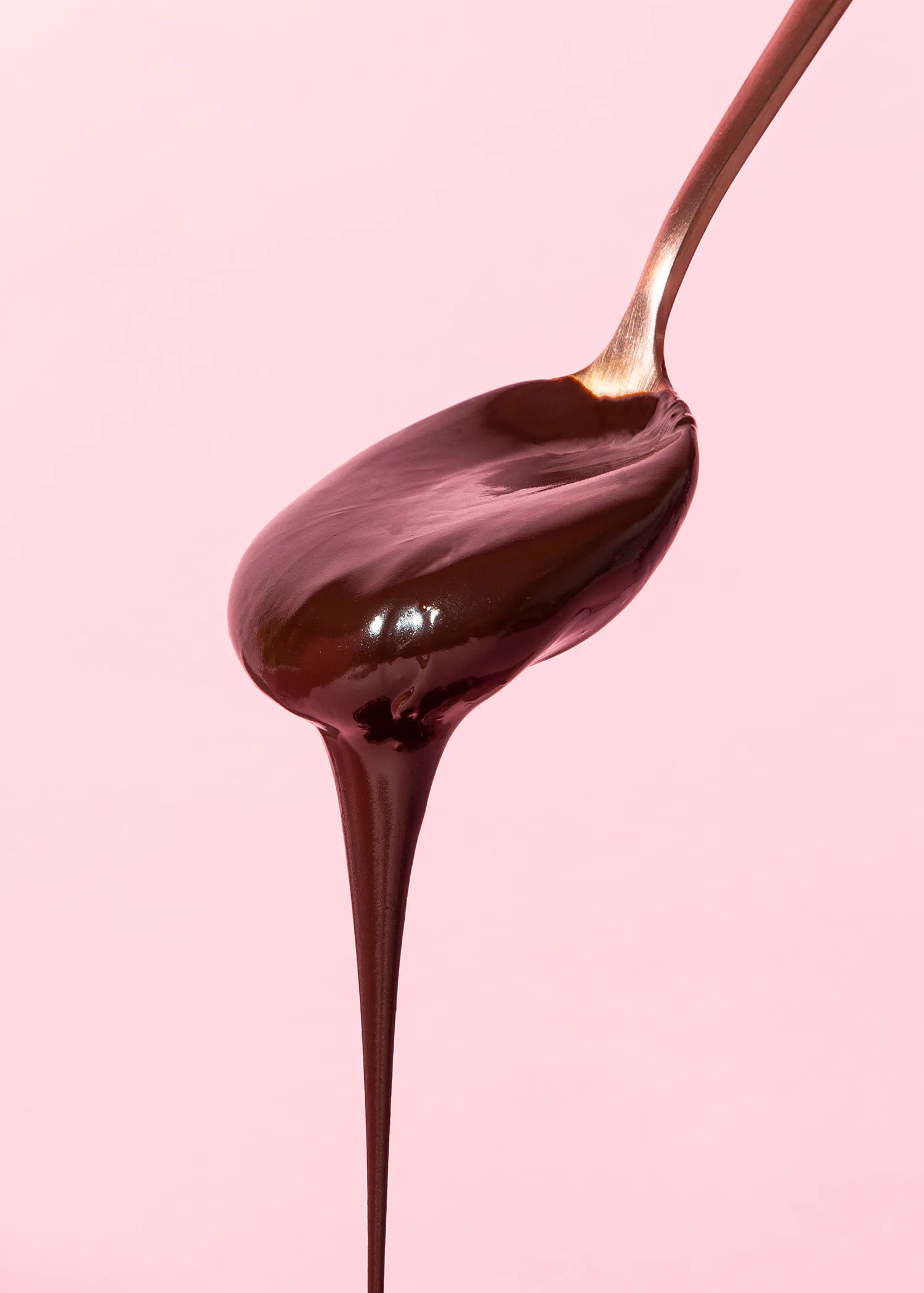 ein löffel mit schmelzender schokolade, die vor einem rosa hintergrund heruntertropft.