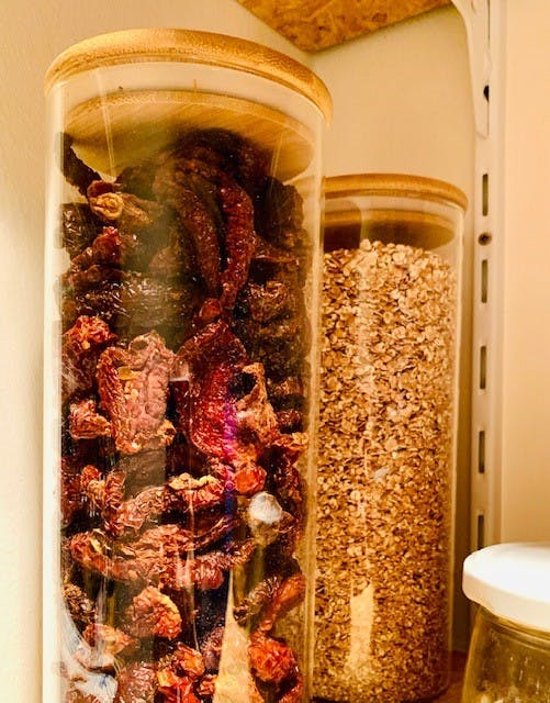 a glass jar filled with dried tomatoes and oats on a shelf .