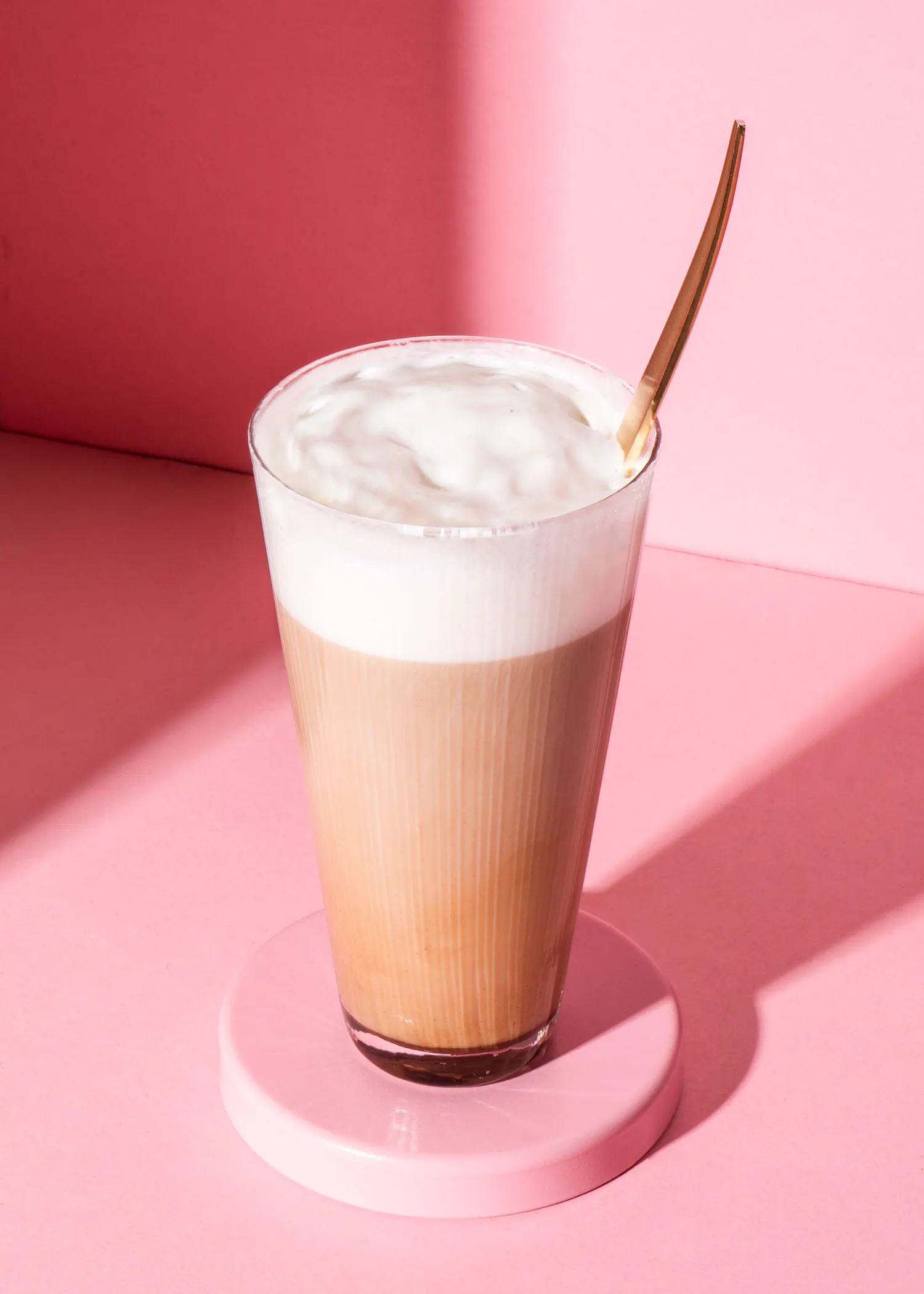 un verre de café avec une cuillère en or sur une table rose