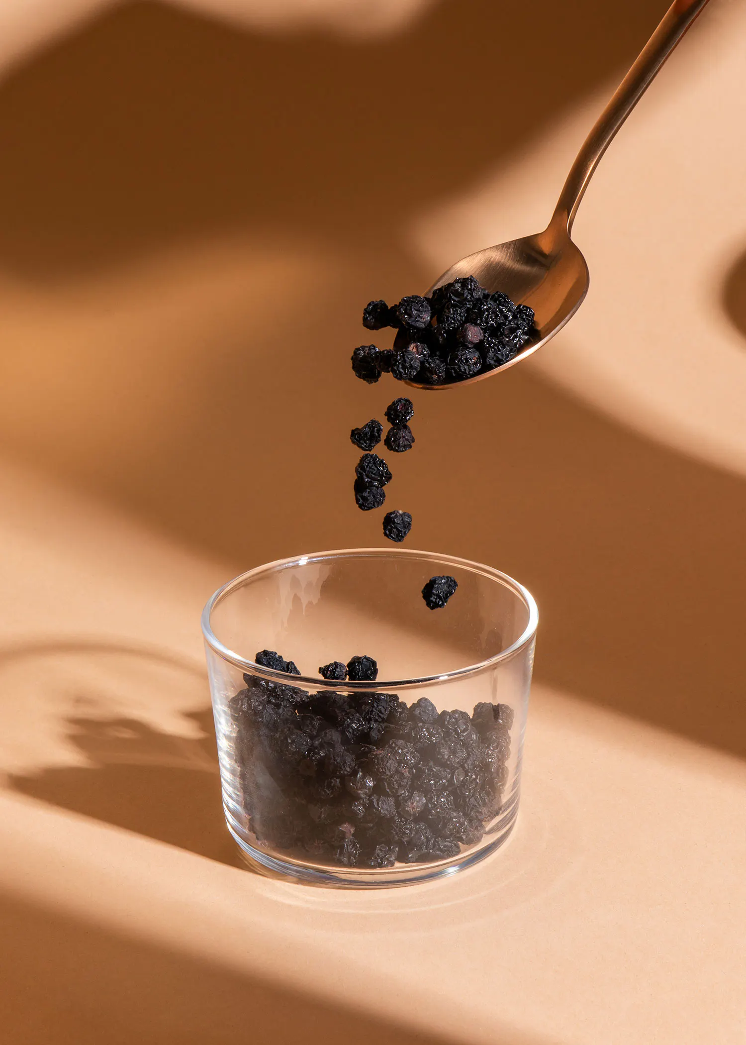 une cuillère remplie de baies noires est versée dans un bol en verre
