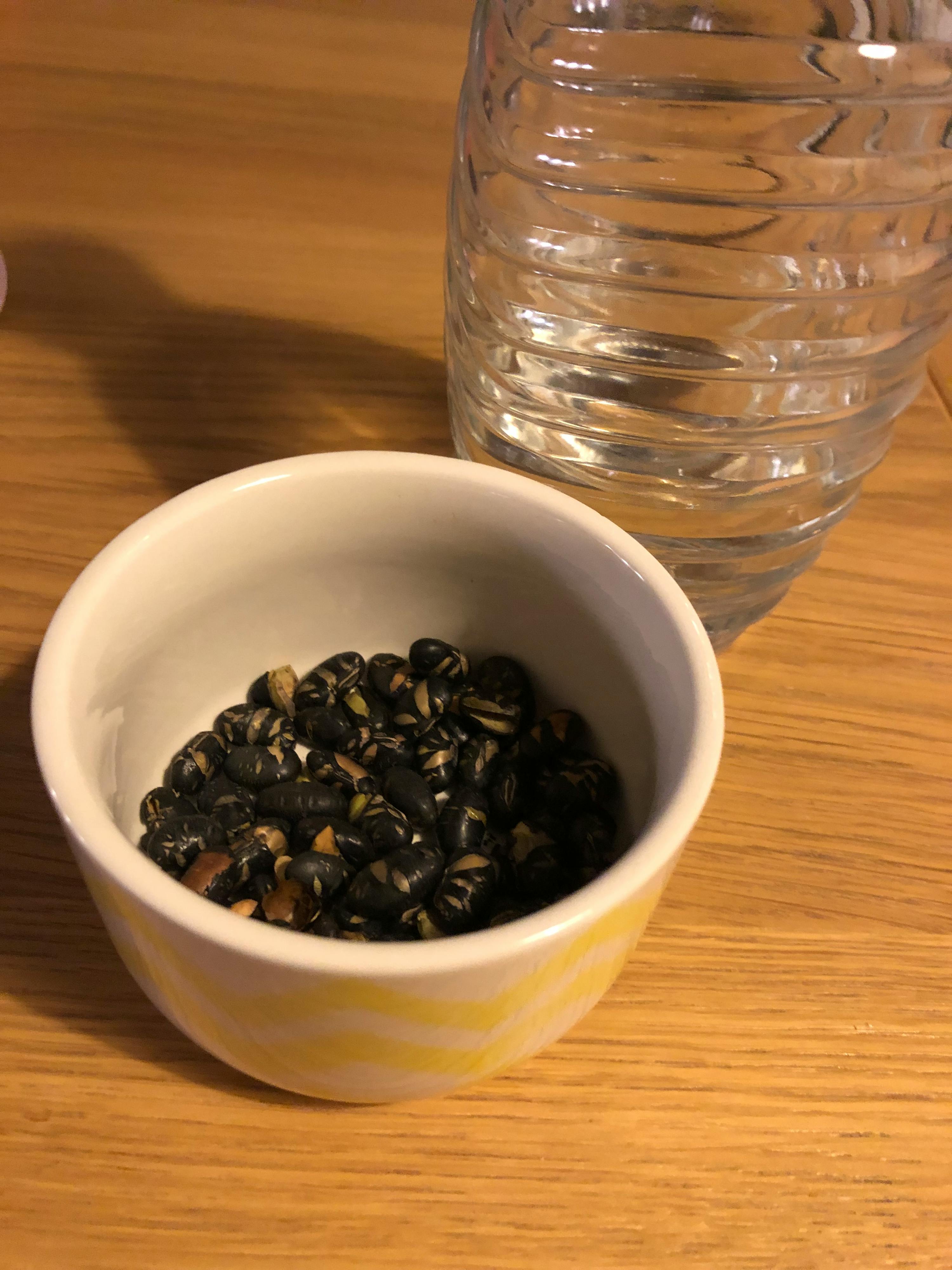 eine kleine weiße und gelbe Schüssel mit schwarzen Bohnen neben einer Flasche Wasser