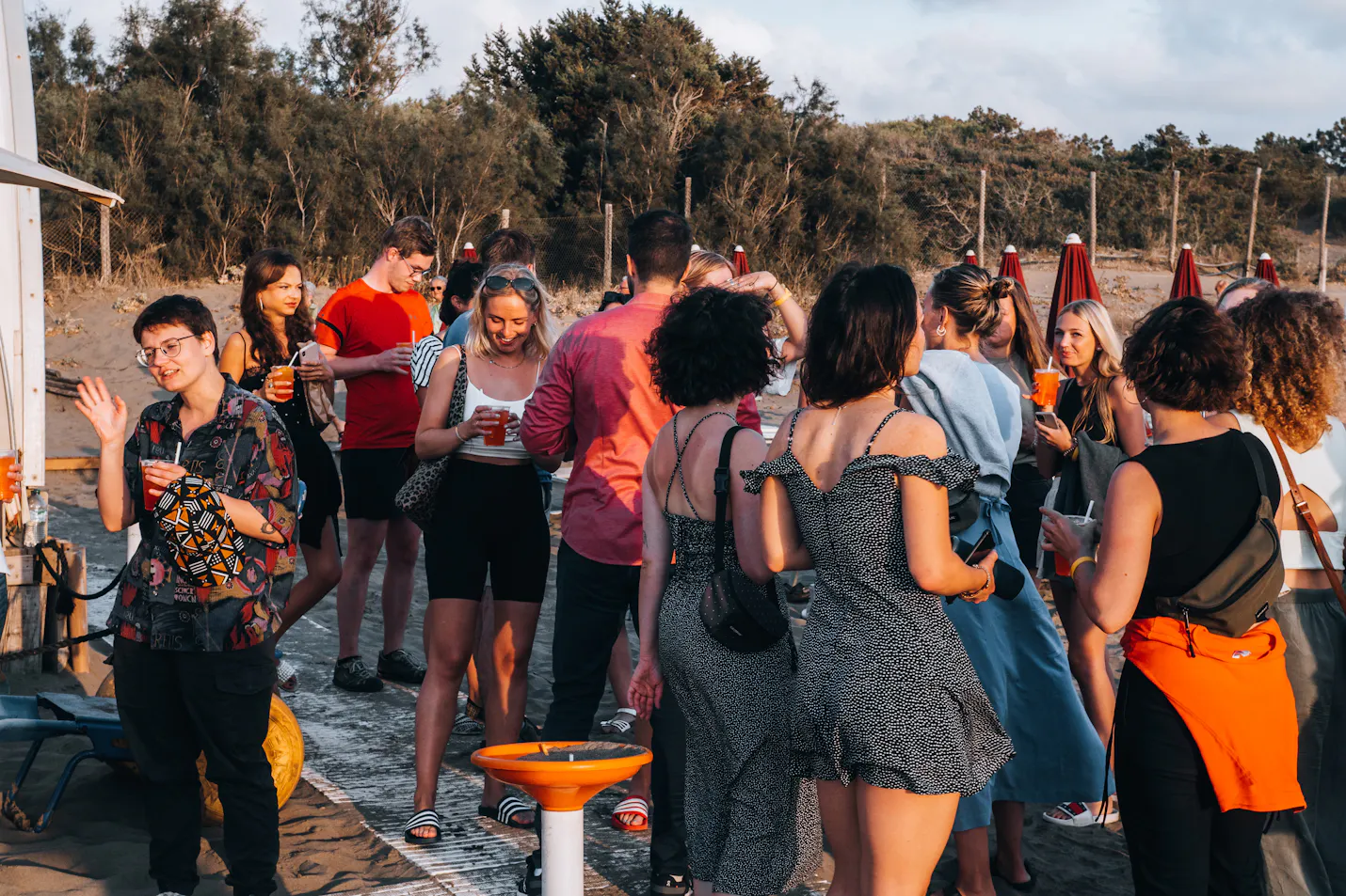 un groupe de personnes se rassemblent sur une plage avec des boissons dans leurs mains