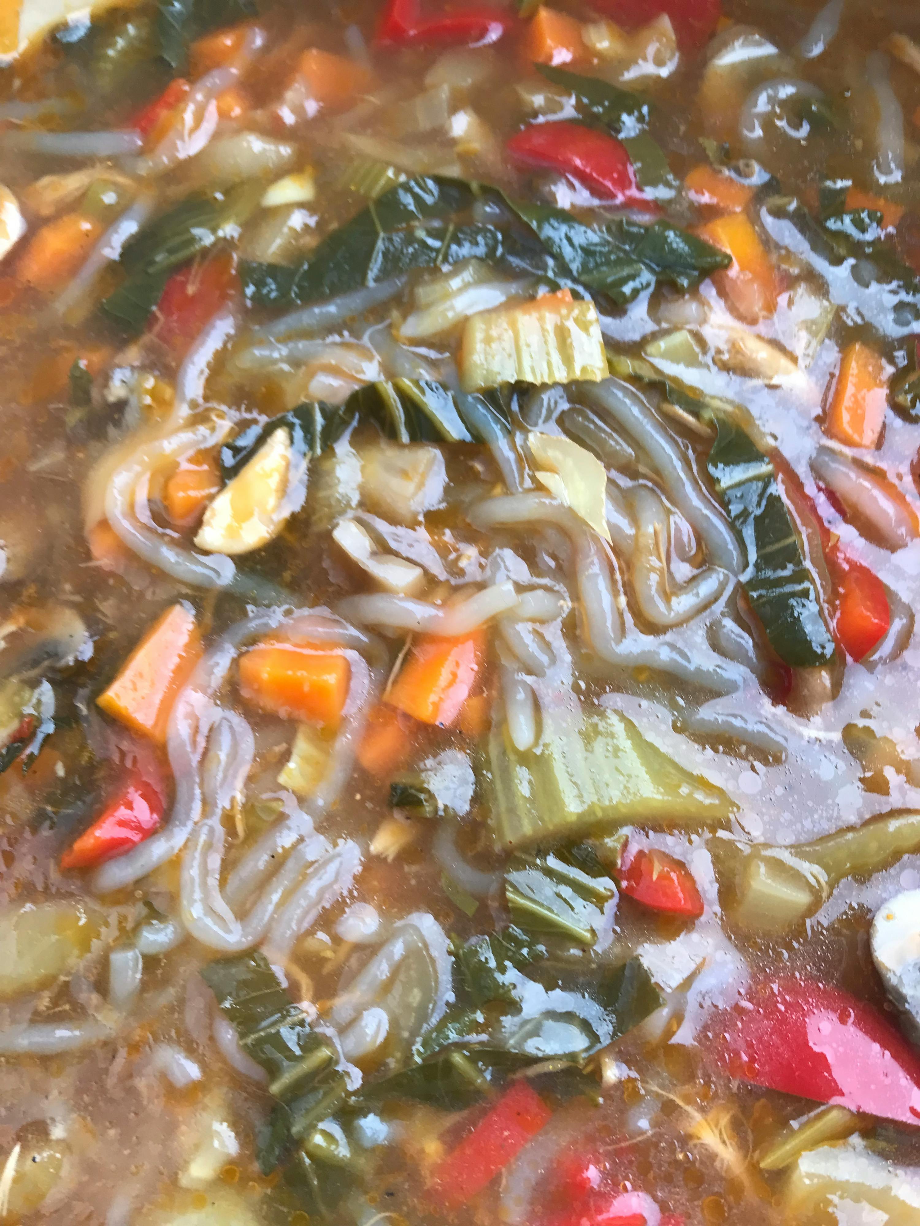 a close up of a soup with vegetables and noodles