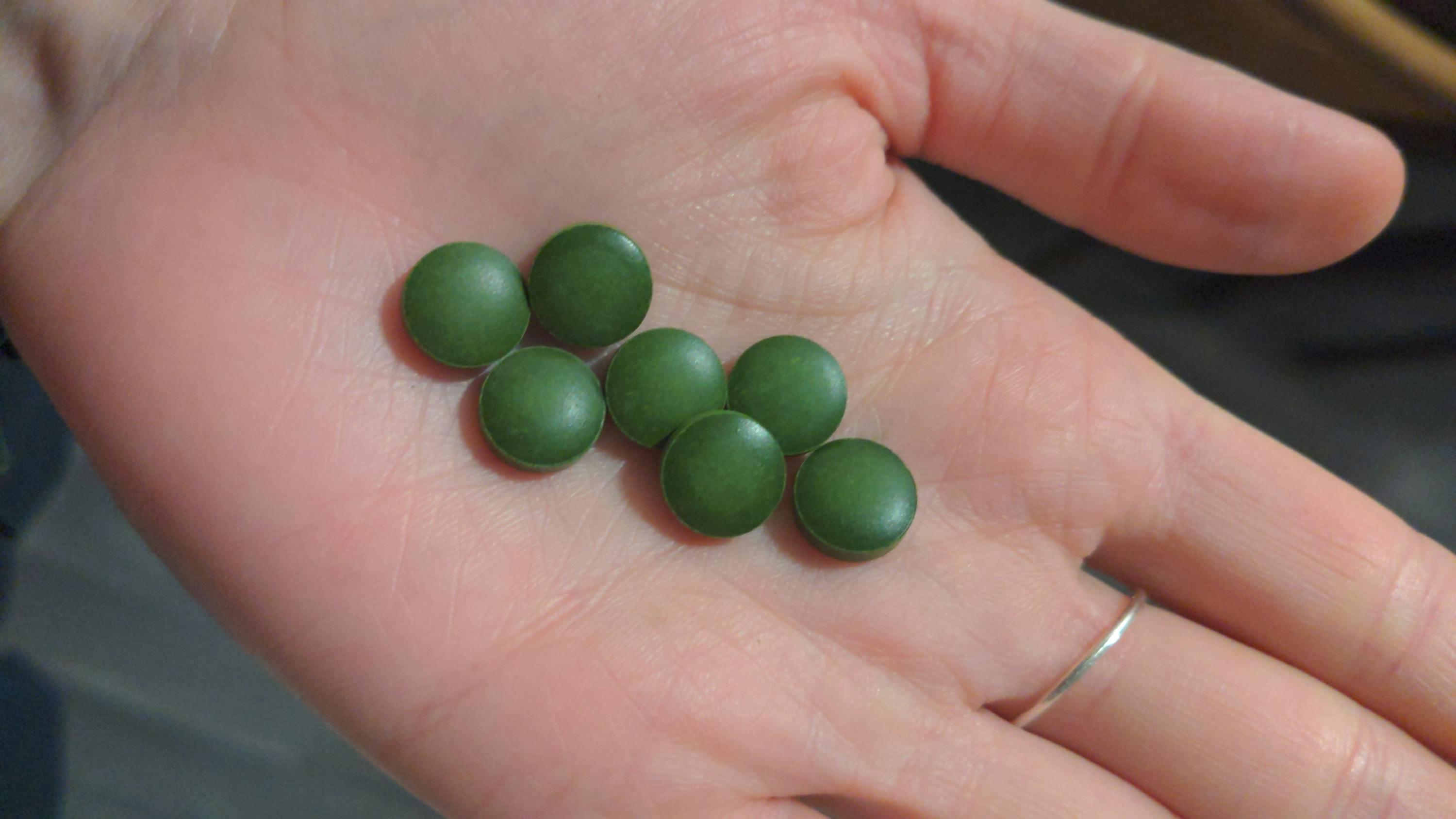 une personne tient dans sa main un tas de pilules vertes