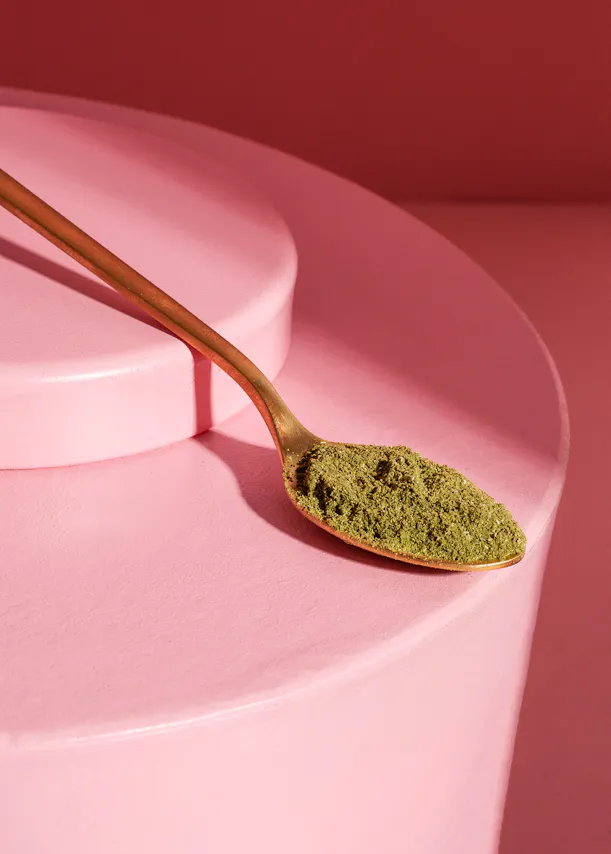 ein goldener Löffel mit grünempulver auf einem rosa Hintergrund