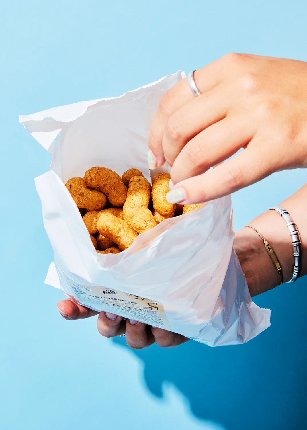 une personne tient un sac blanc rempli de nuggets de poulet sur fond bleu