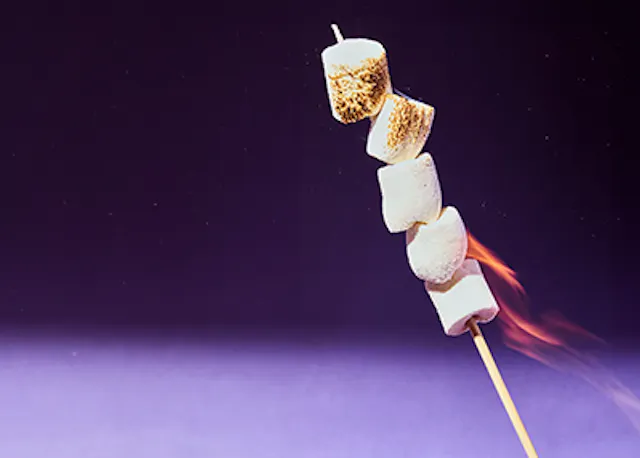 Marshmallows auf einem Holzstab mit Flammen darauf