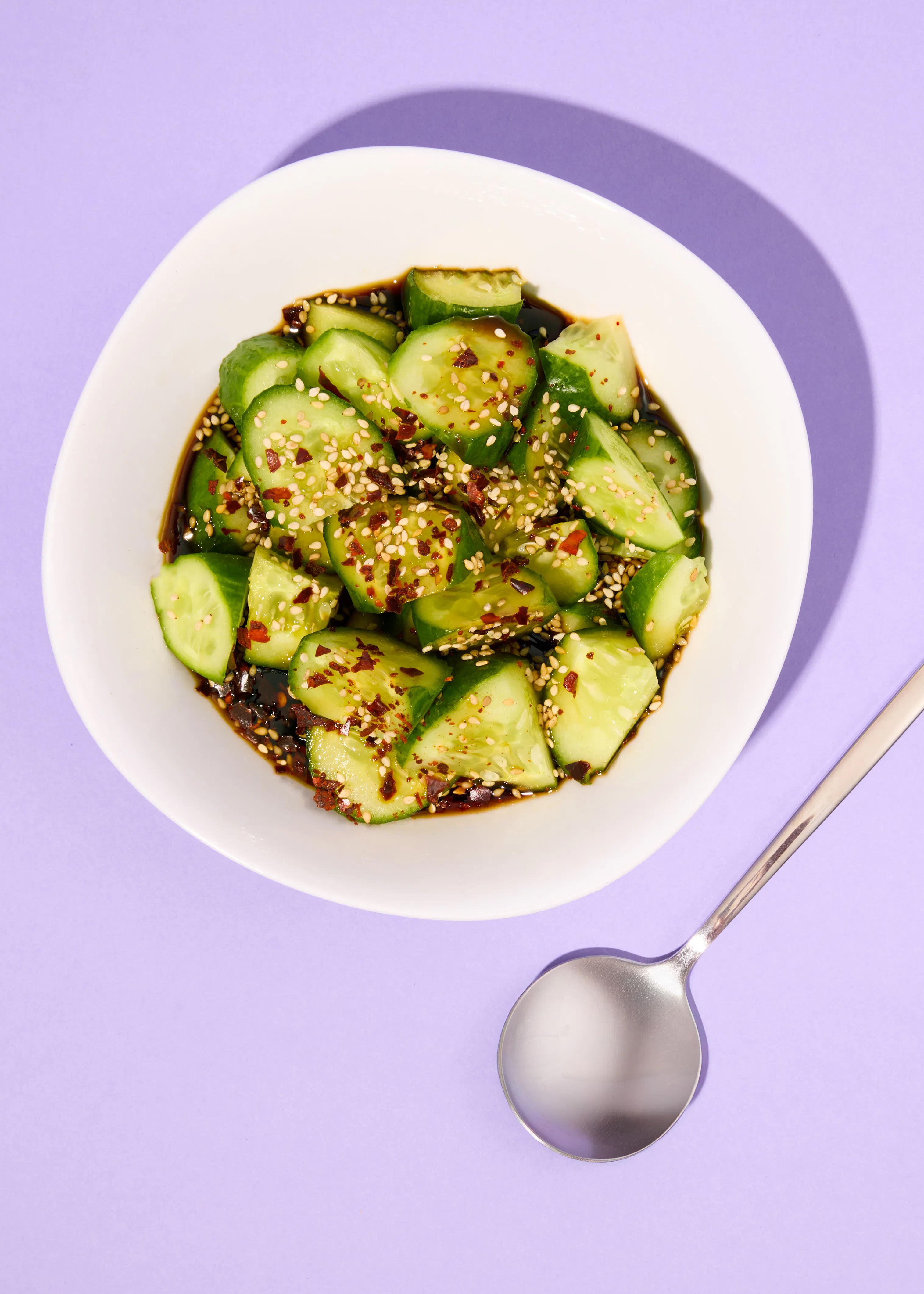a bowl of cucumber salad with sesame seeds and sauce next to a spoon