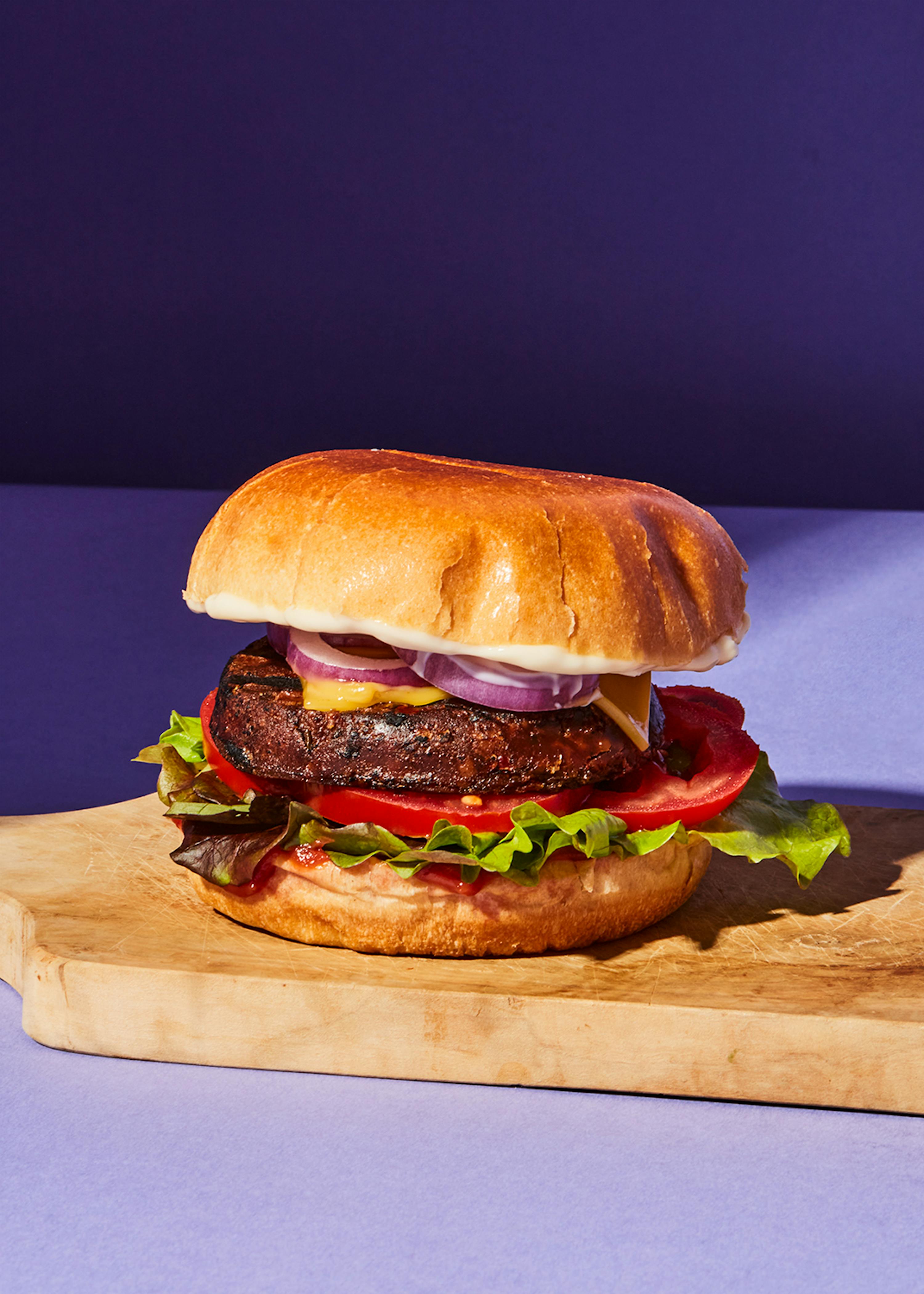 una hamburguesa con tomates y ensalada está sobre una tabla de cortar de madera