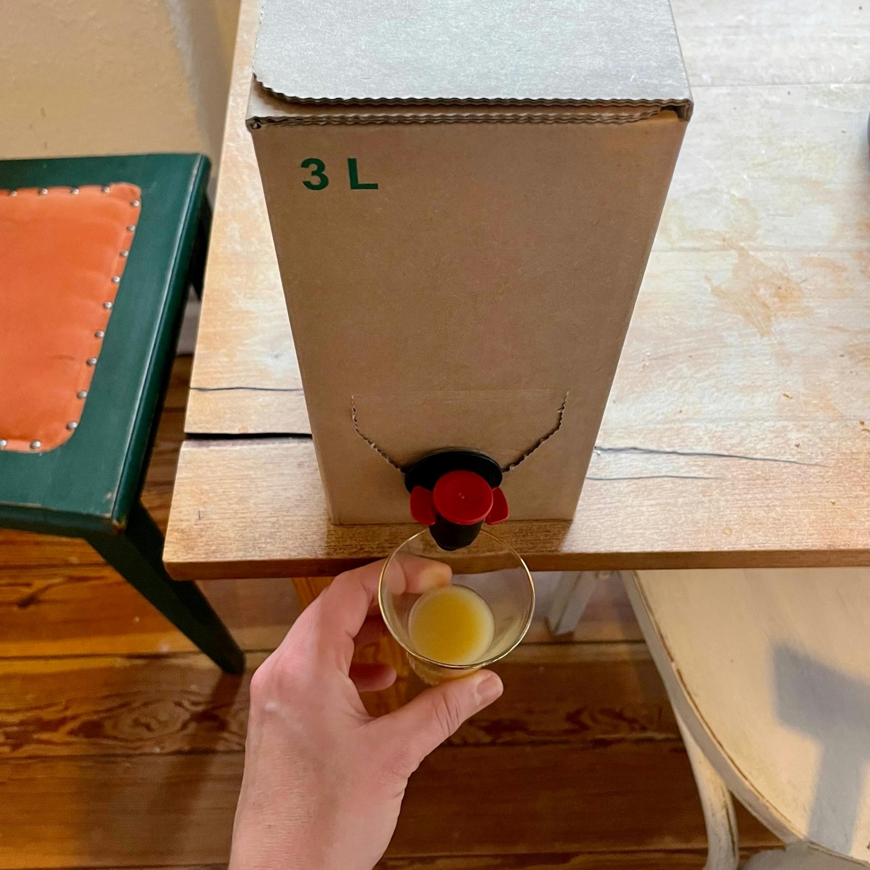 Eine Person hält ein Glas vor einer 3l-Box