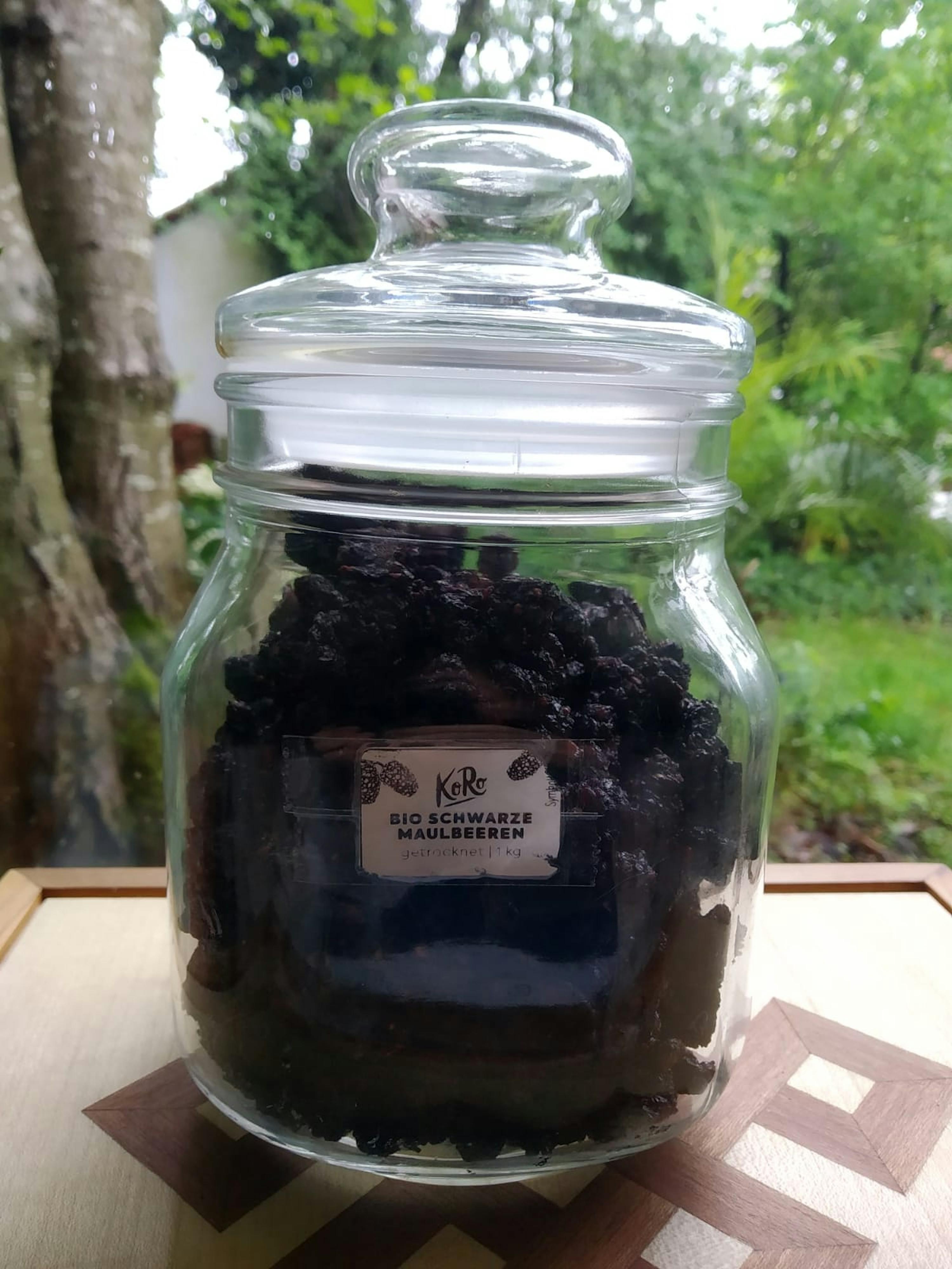 ein Glas mit schwarzen Maulbeeren steht auf einem Holztisch