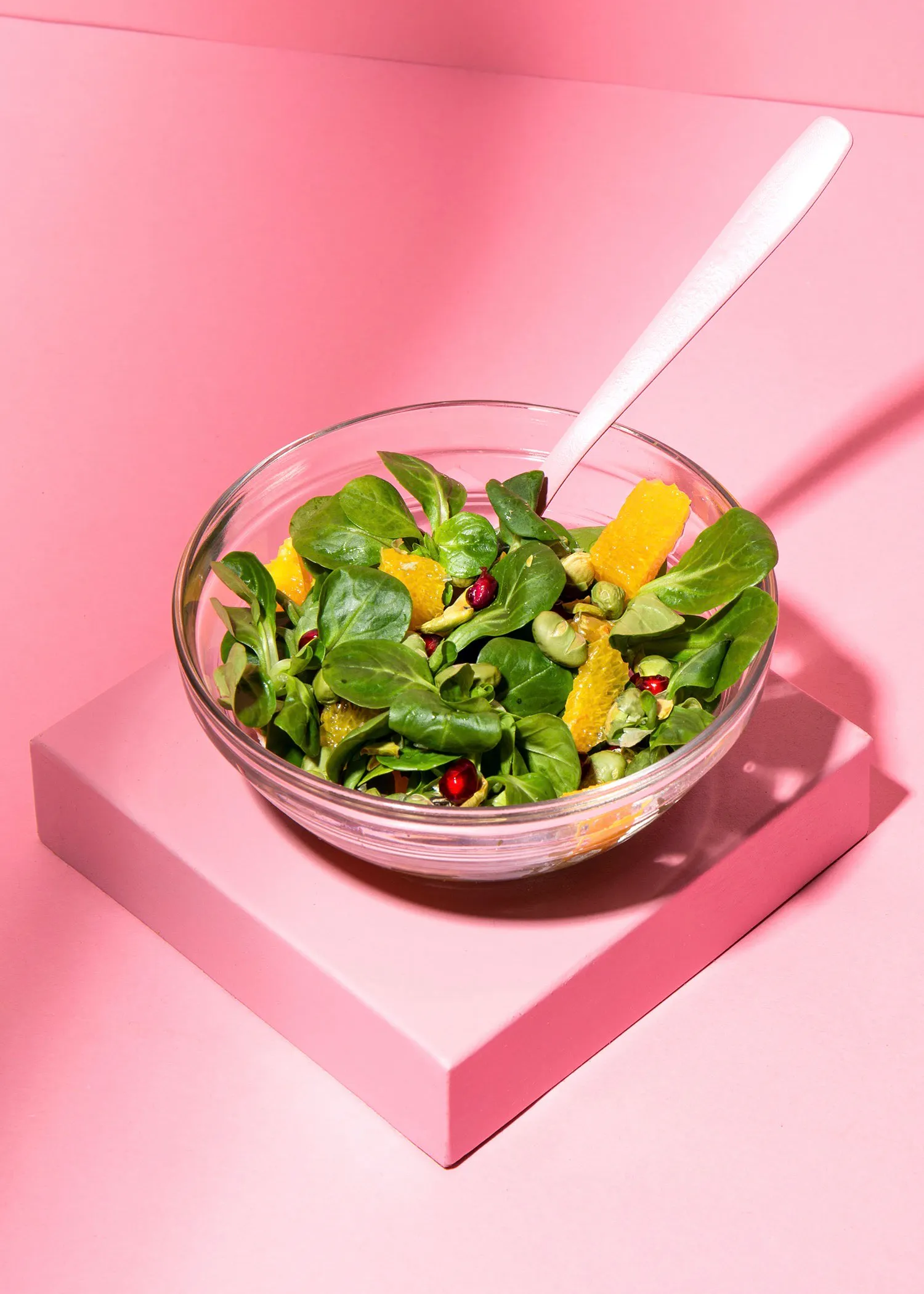 un bol de salade avec une cuillère sur une surface rose
