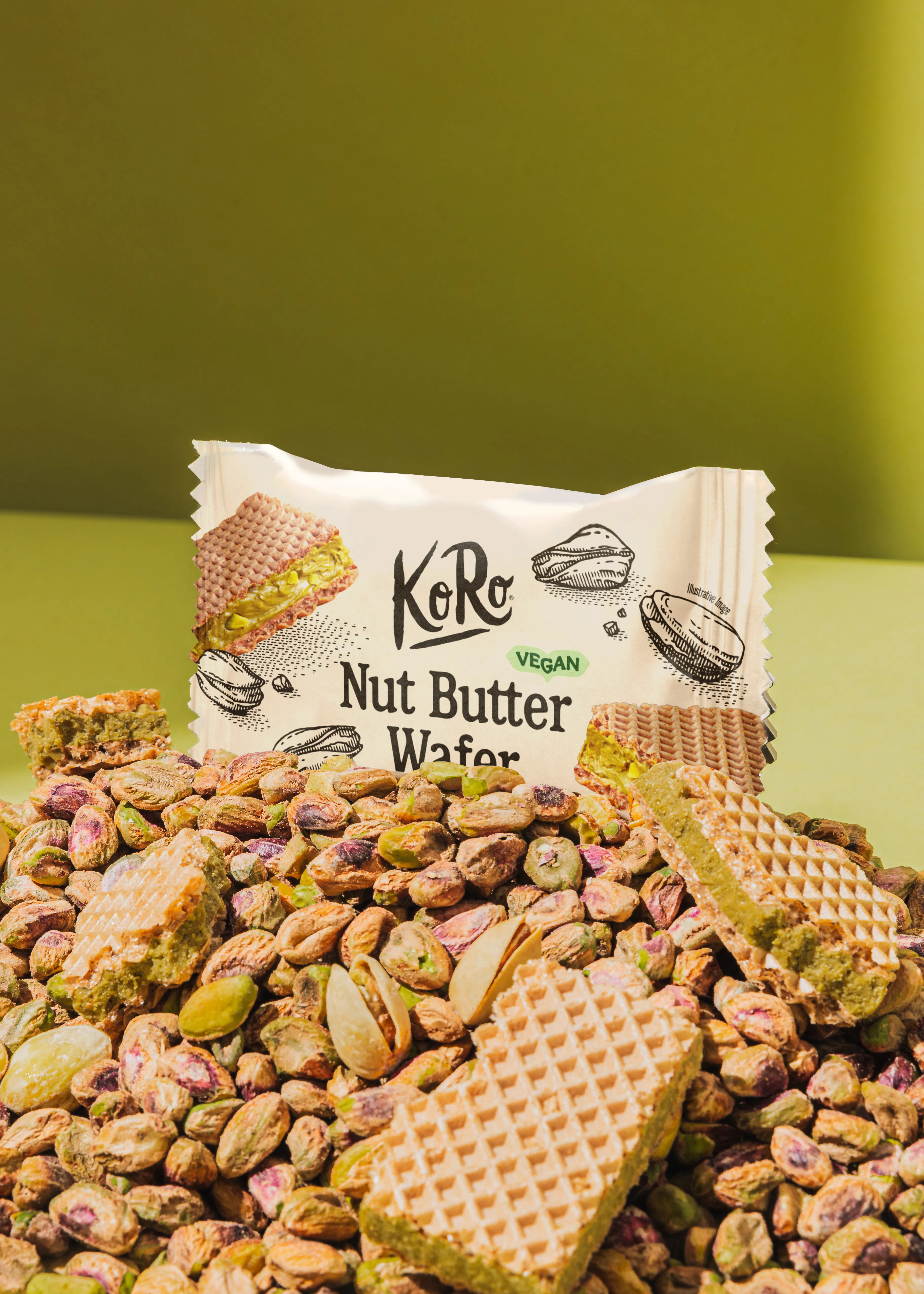 eine packung koro veganer nussbutter-waffel liegt auf einem haufen ganzer pistazien.