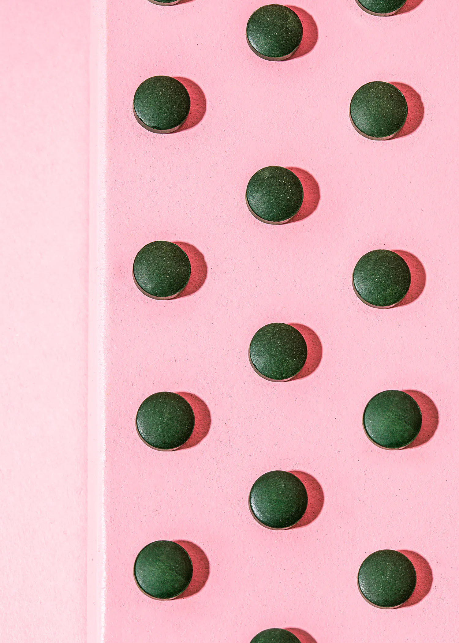 a row of green pills on a pink background