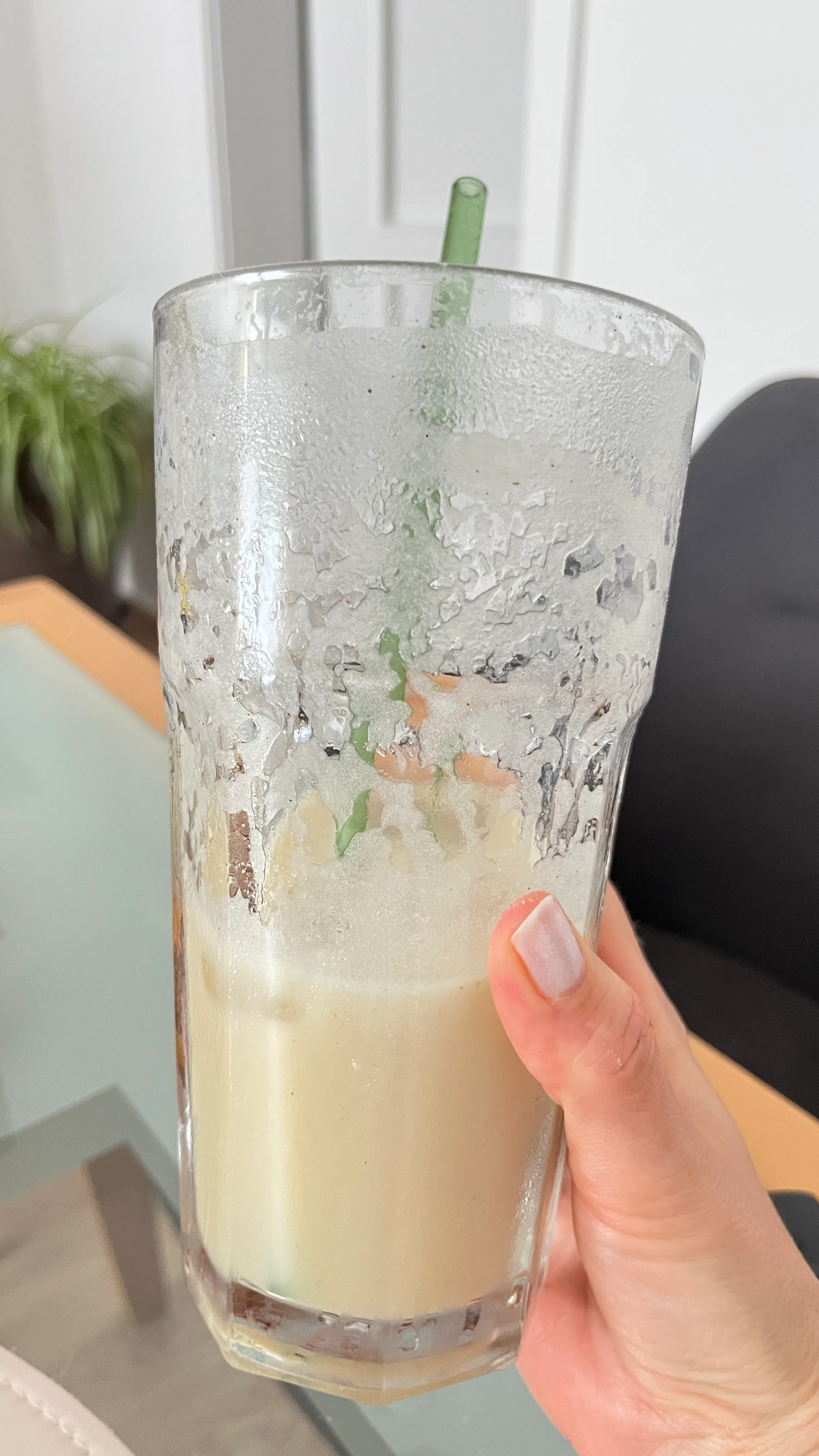 une main tient un verre givré contenant une boisson claire partiellement consommée avec une paille verte.