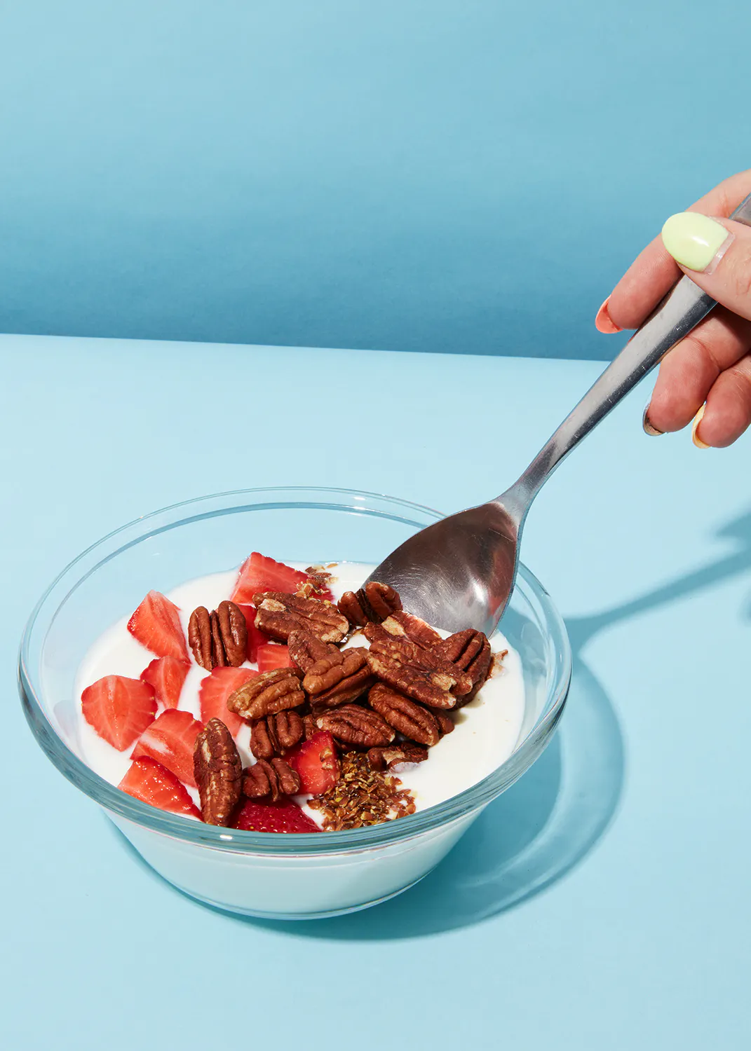 a bowl of yogurt with strawberries and pecans is being scooped with a spoon