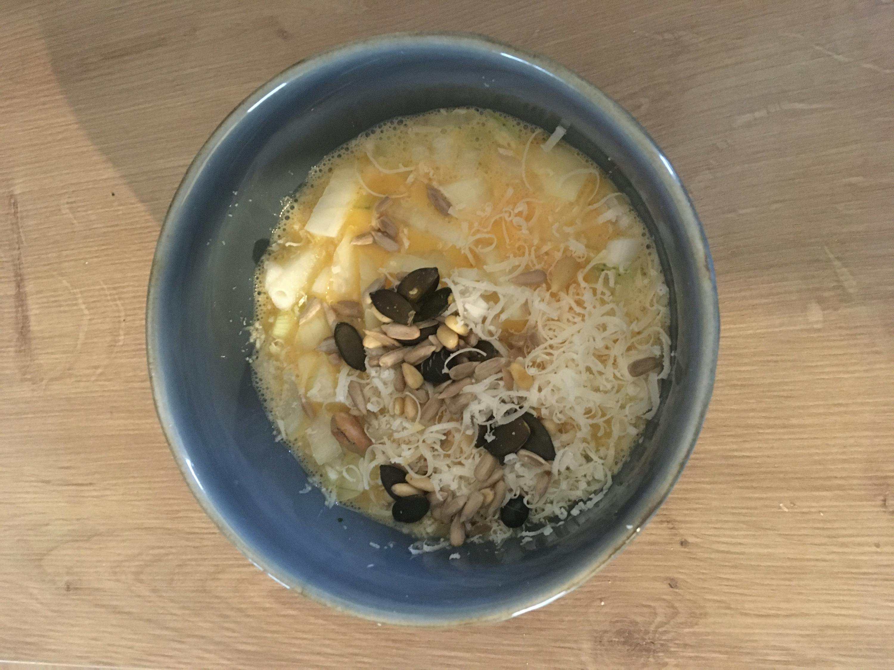 a bowl of soup with nuts and cheese on a wooden table
