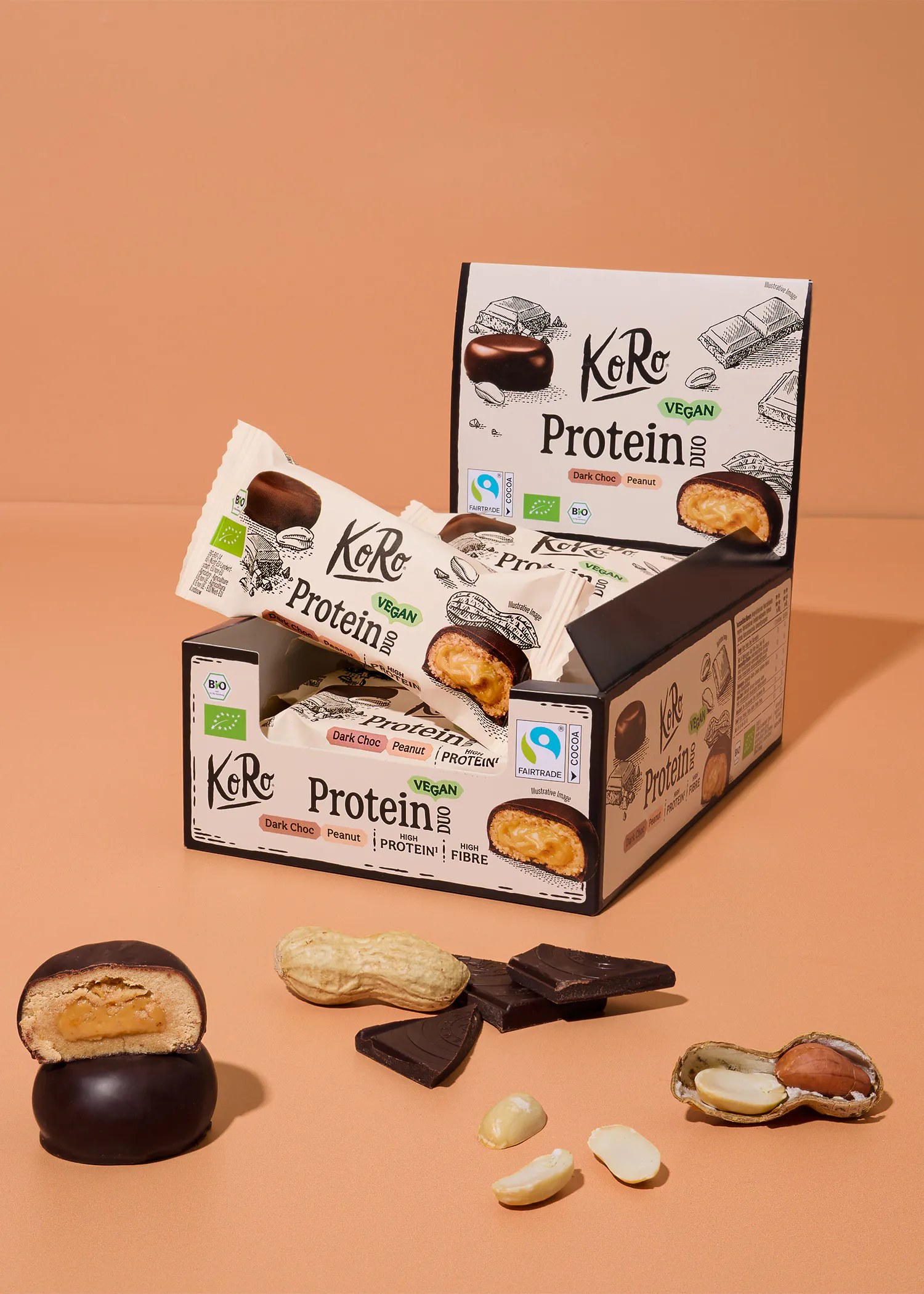 eine geöffnete verkaufsverpackung mit koro protein duo riegeln in der geschmacksrichtung dark choc peanut, davor liegen ein aufgeschnittener riegel, erdnüsse und schokoladenstücke auf einem beigen hintergrund.