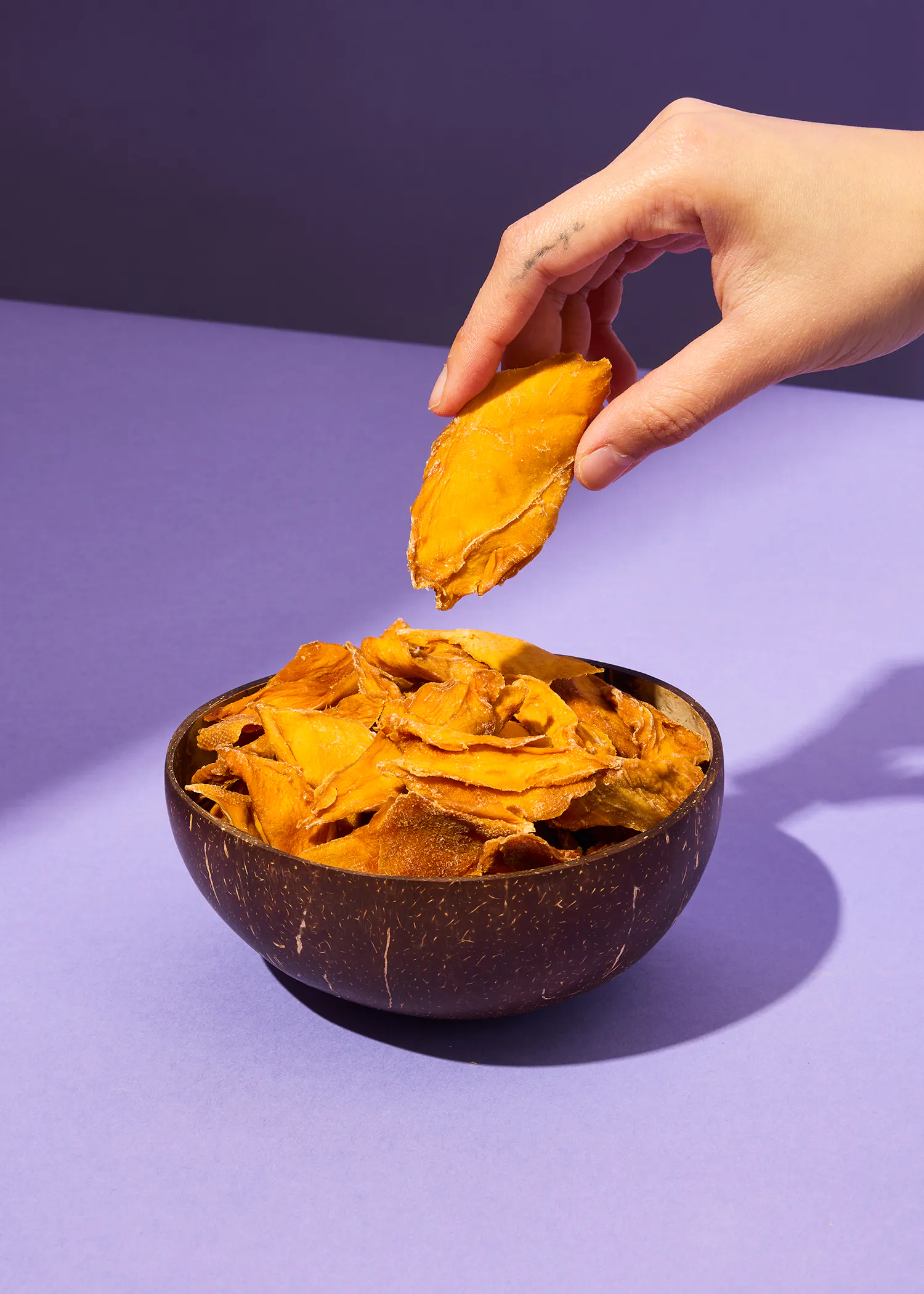 eine Person nimmt eine Scheibe aus einer Schüssel mit getrockneten Früchten