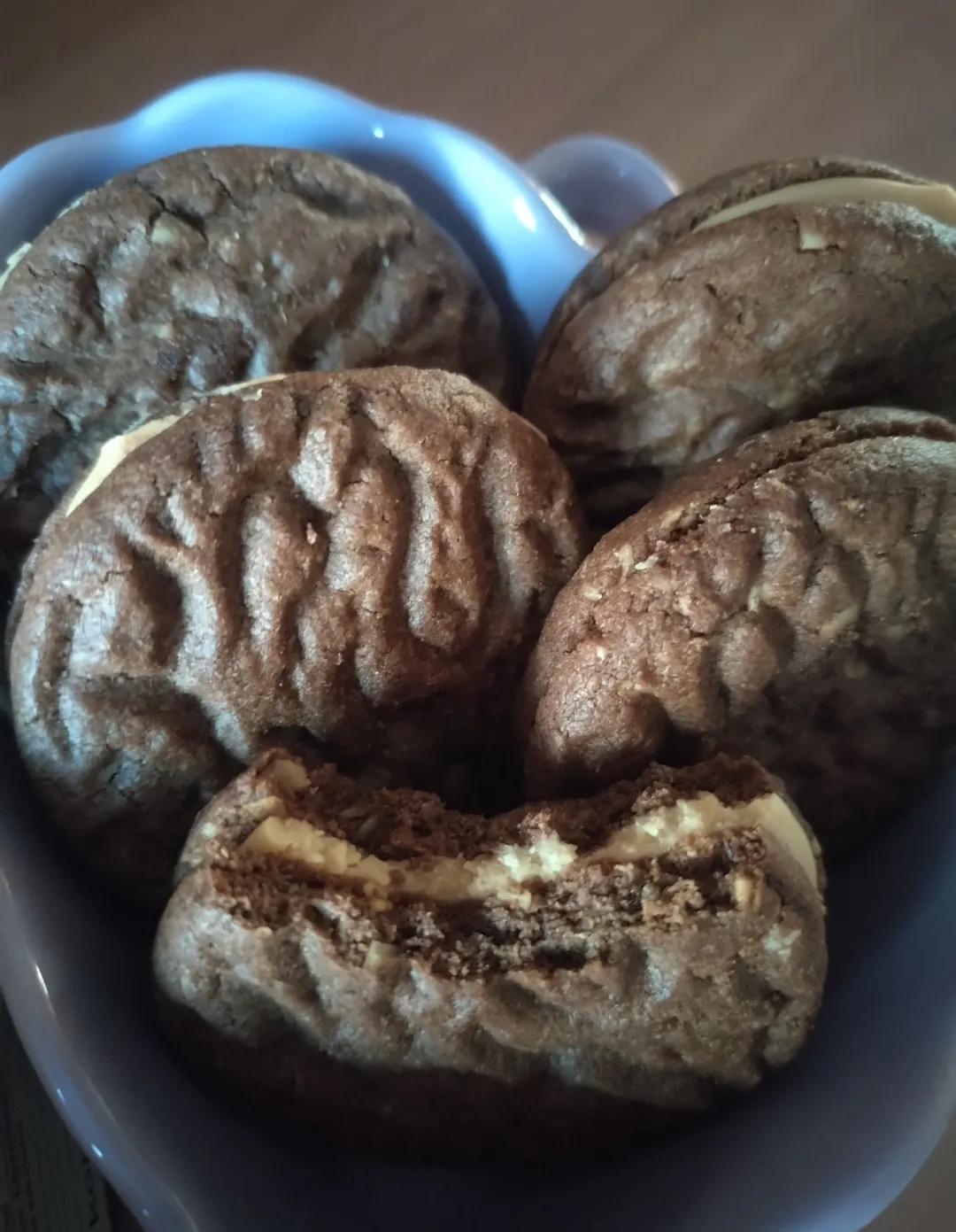 primo piano di alcuni biscotti al cacao farciti con crema chiara disposti in una ciotola azzurra.