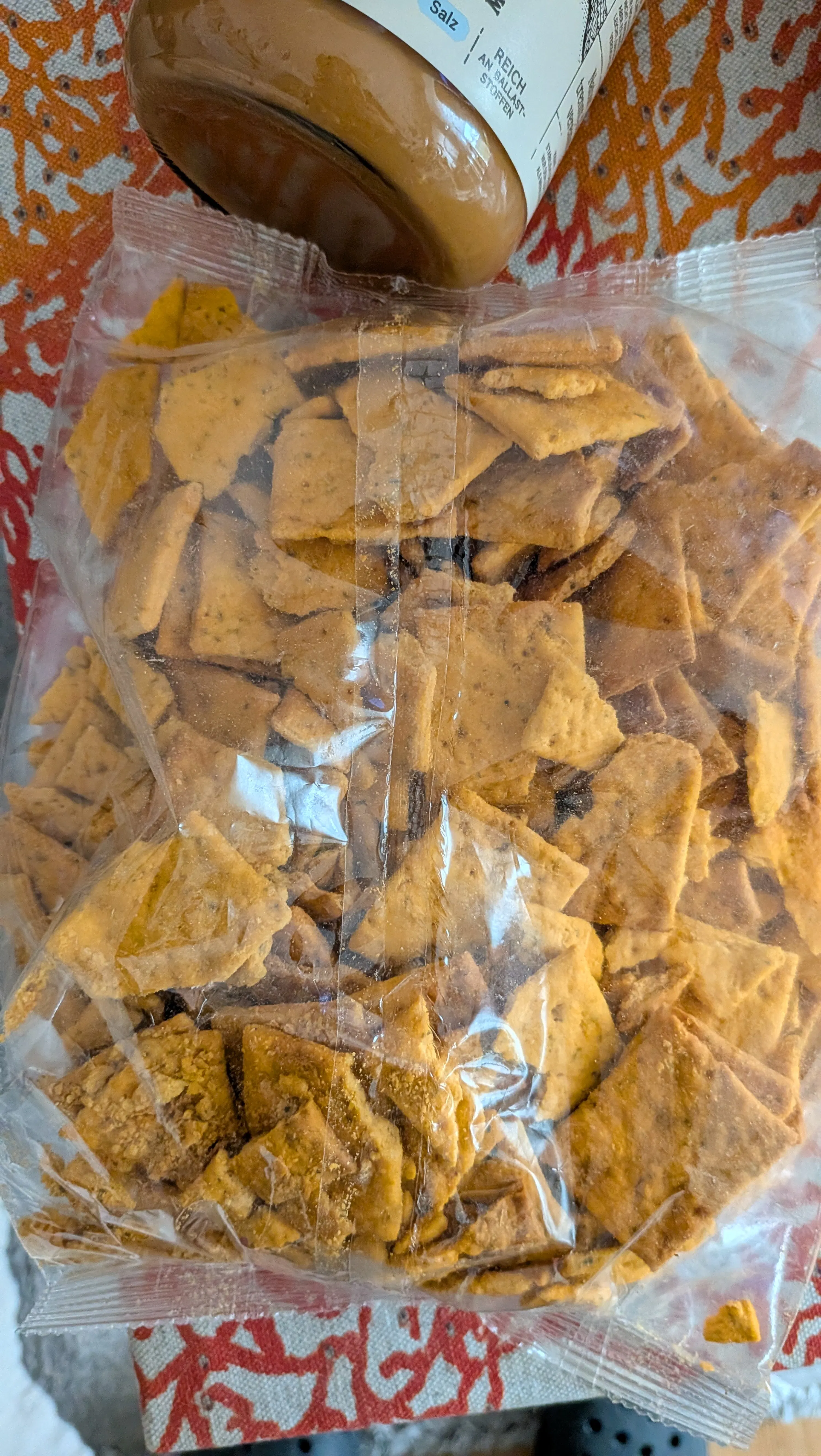 eine offene, durchsichtige plastiktüte ist mit vielen unregelmäßig geformten, goldbraunen, gewürzten crackers gefüllt, mit dem boden einer braunen flasche im hintergrund.