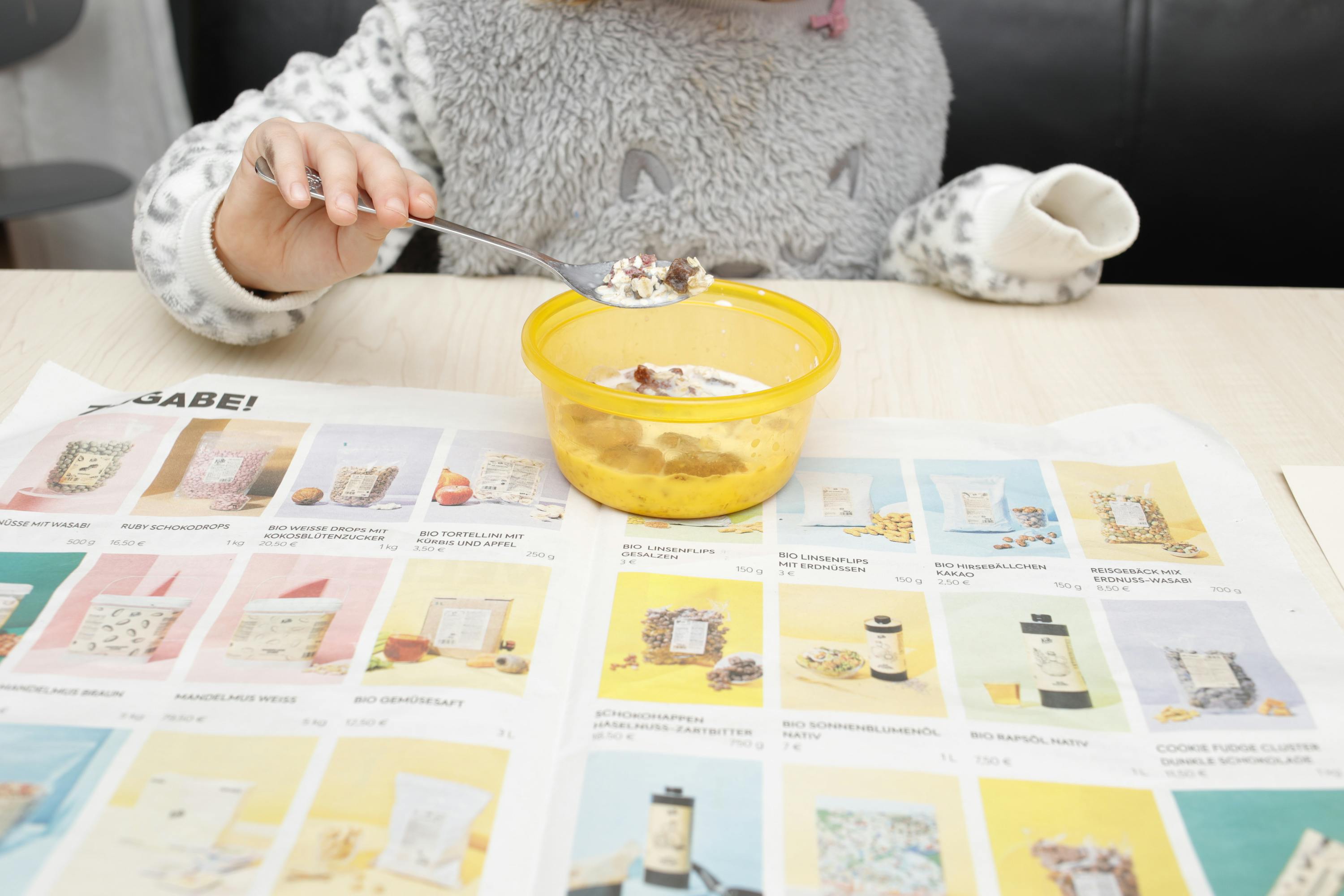 une petite fille mange un bol de céréales avec une cuillère sur une table