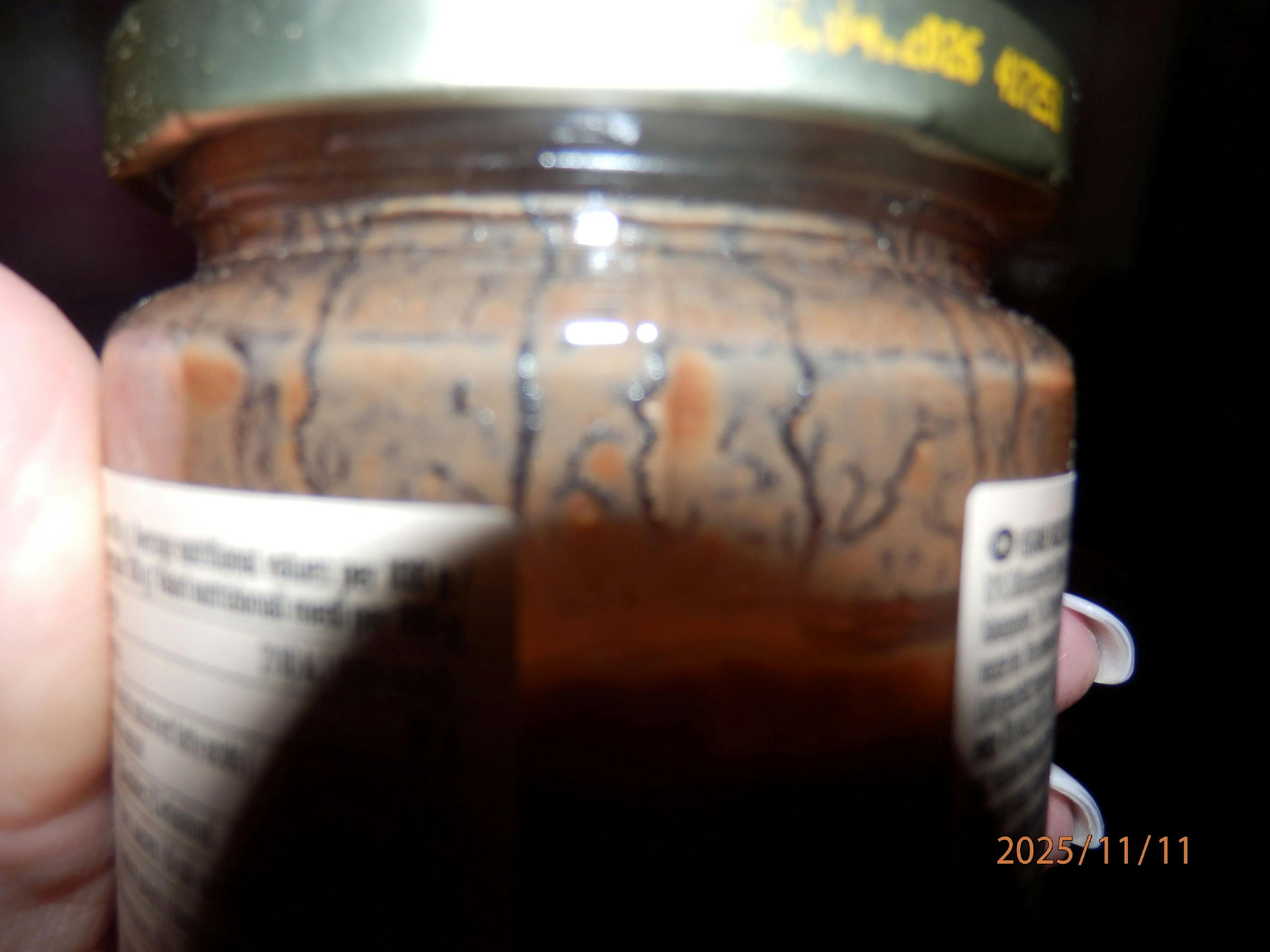 ein unscharfes nahaufnahmebild eines glases mit einer braunen, strukturierten paste und einem grünen deckel, das von einer hand gehalten wird.