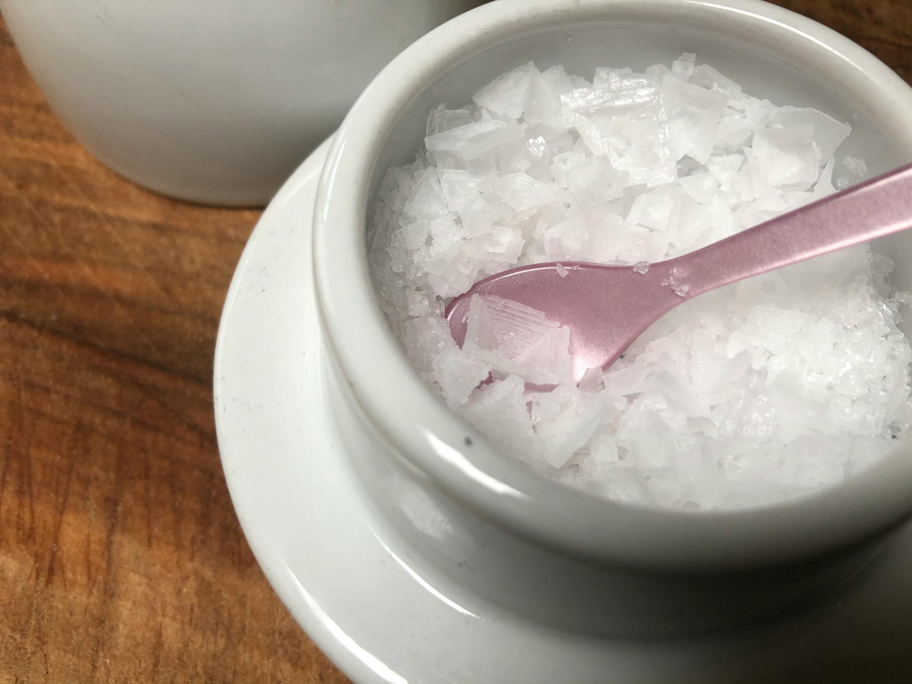 eine weiße Schüssel mit weißem Salz und einem rosa Löffel darin