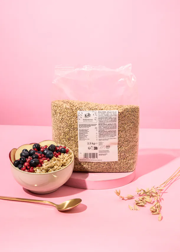 eine Tüte Haferflocken neben einer Schüssel Haferflocken und einem Löffel