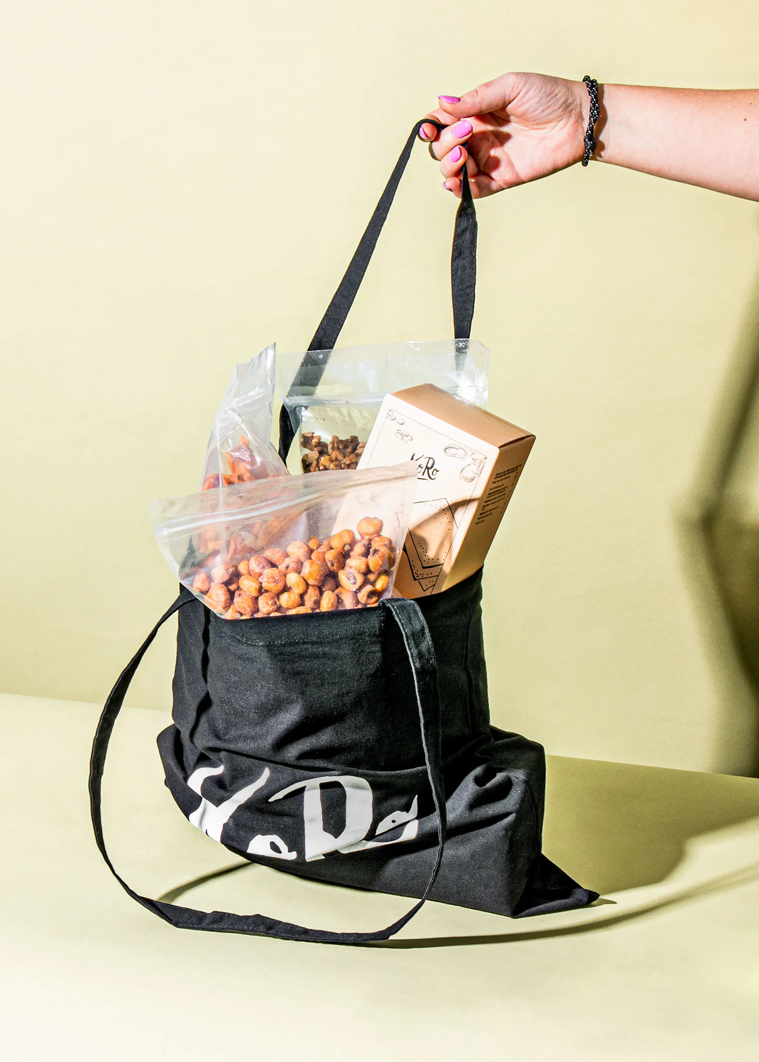 eine Person hält eine schwarze Einkaufstasche mit einer Schachtel Nudeln darin