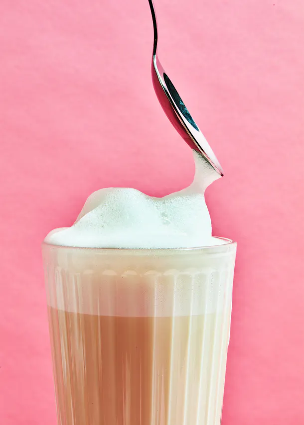 une cuillère verse de la mousse dans un verre de cappuccino
