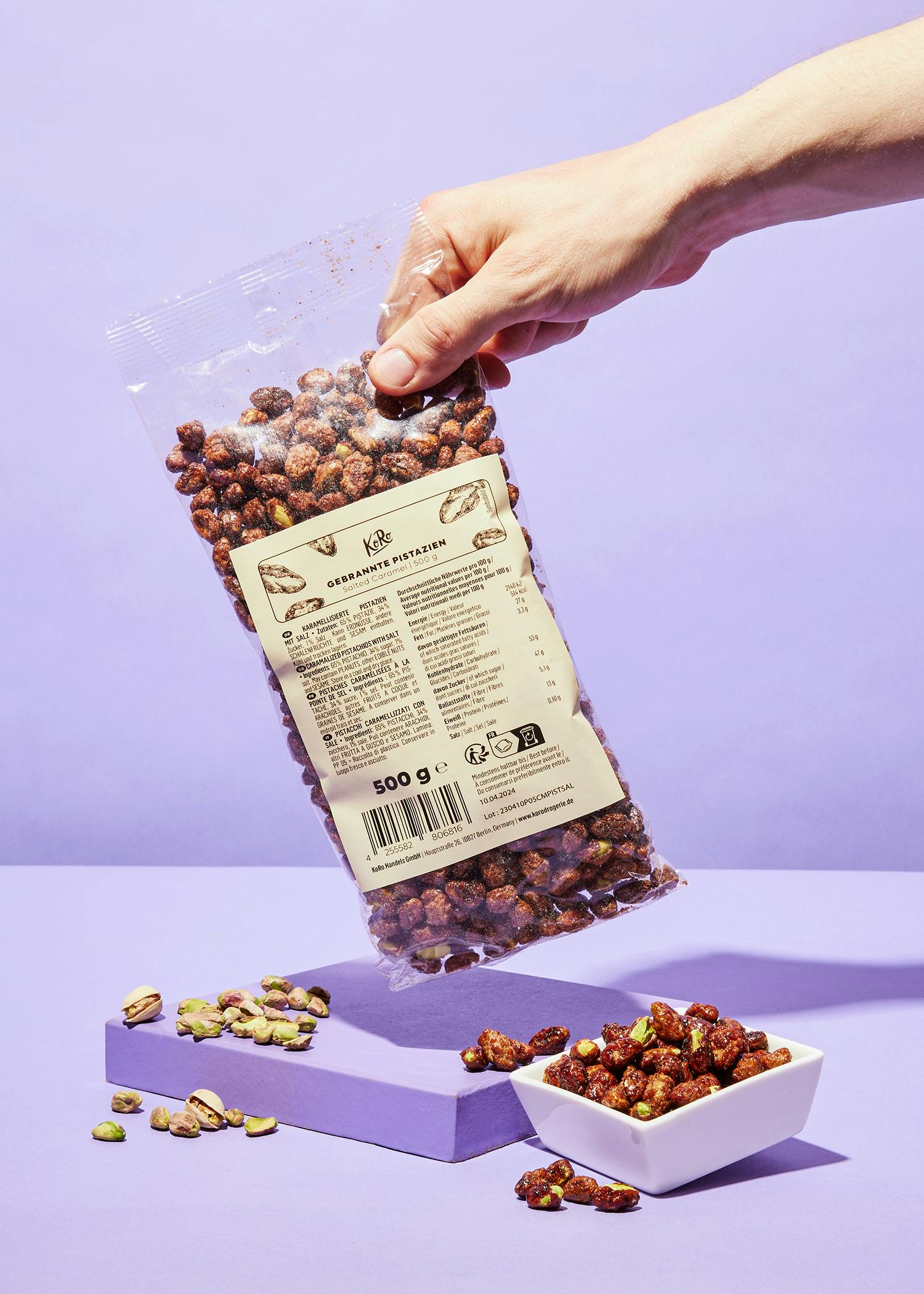 a hand is holding a bag of pistachios on a purple surface