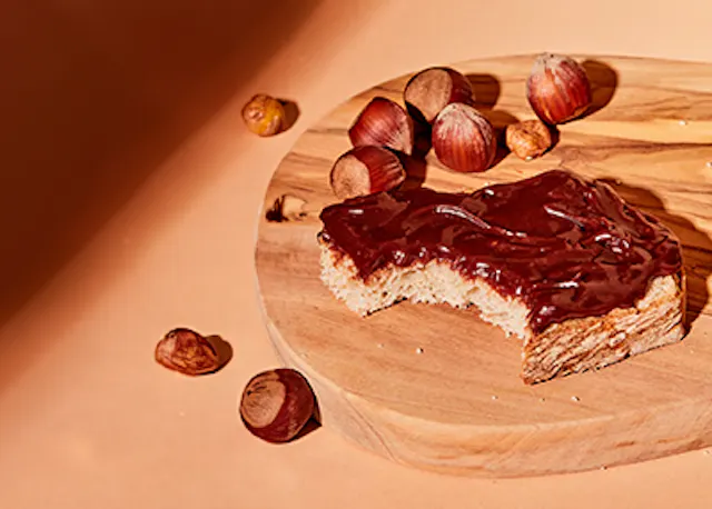 une tranche de pain avec du chocolat et des noisettes sur une planche à découper en bois