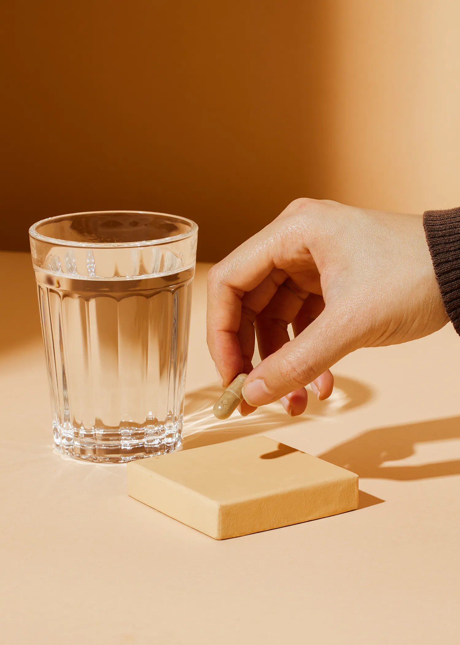 a person taking a capsule next to a glass of water