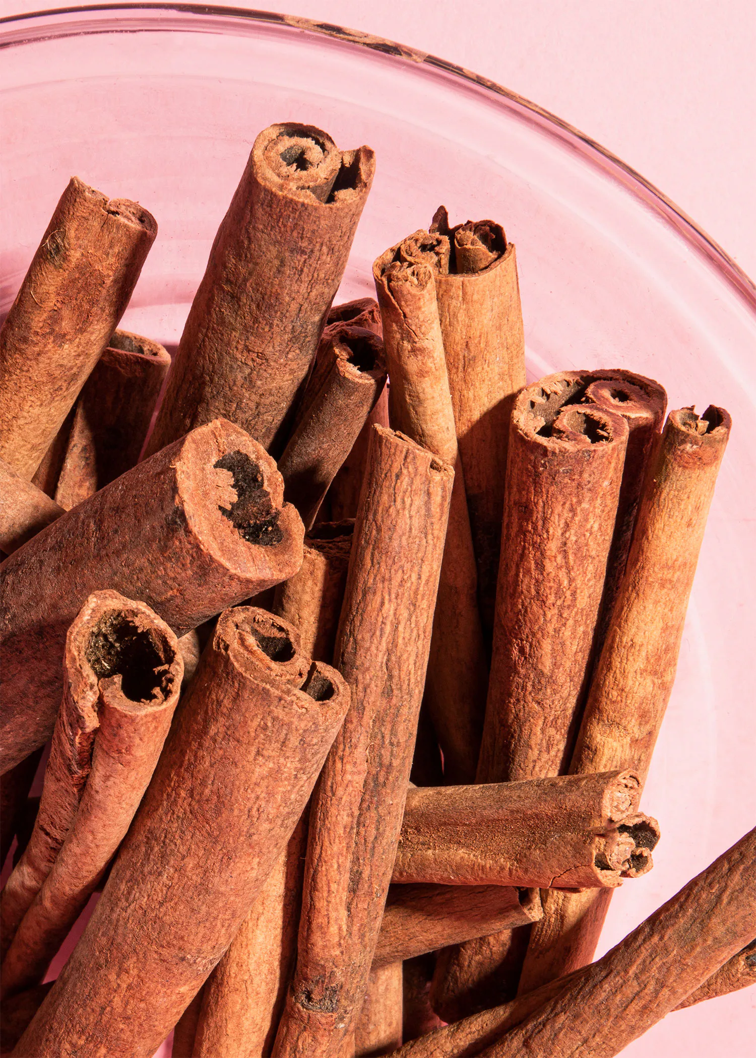 a glass bowl filled with cinnamon sticks on a pink surface