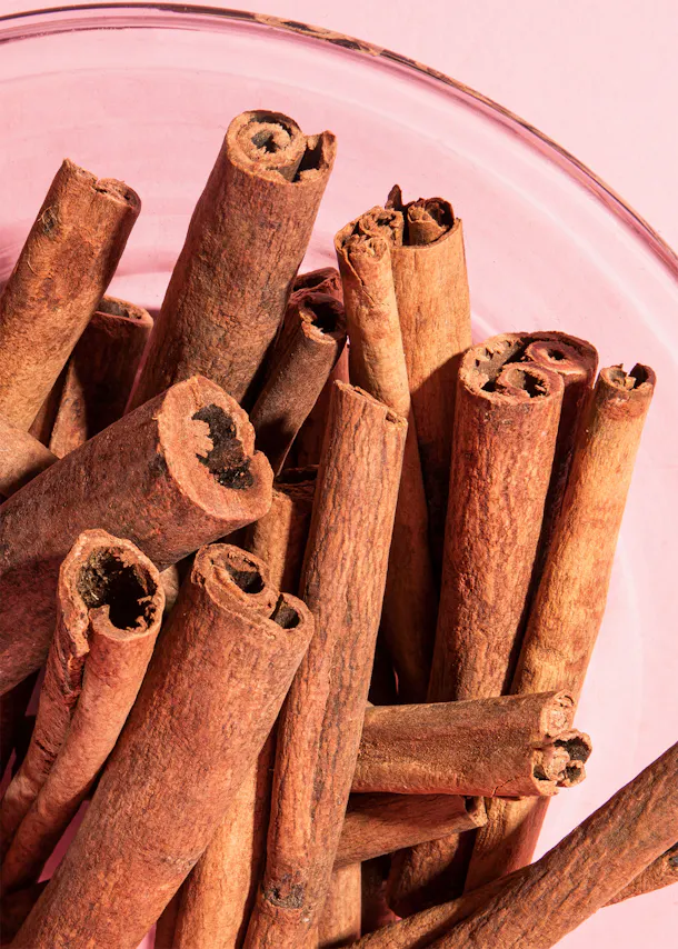 a glass bowl filled with cinnamon sticks on a pink surface