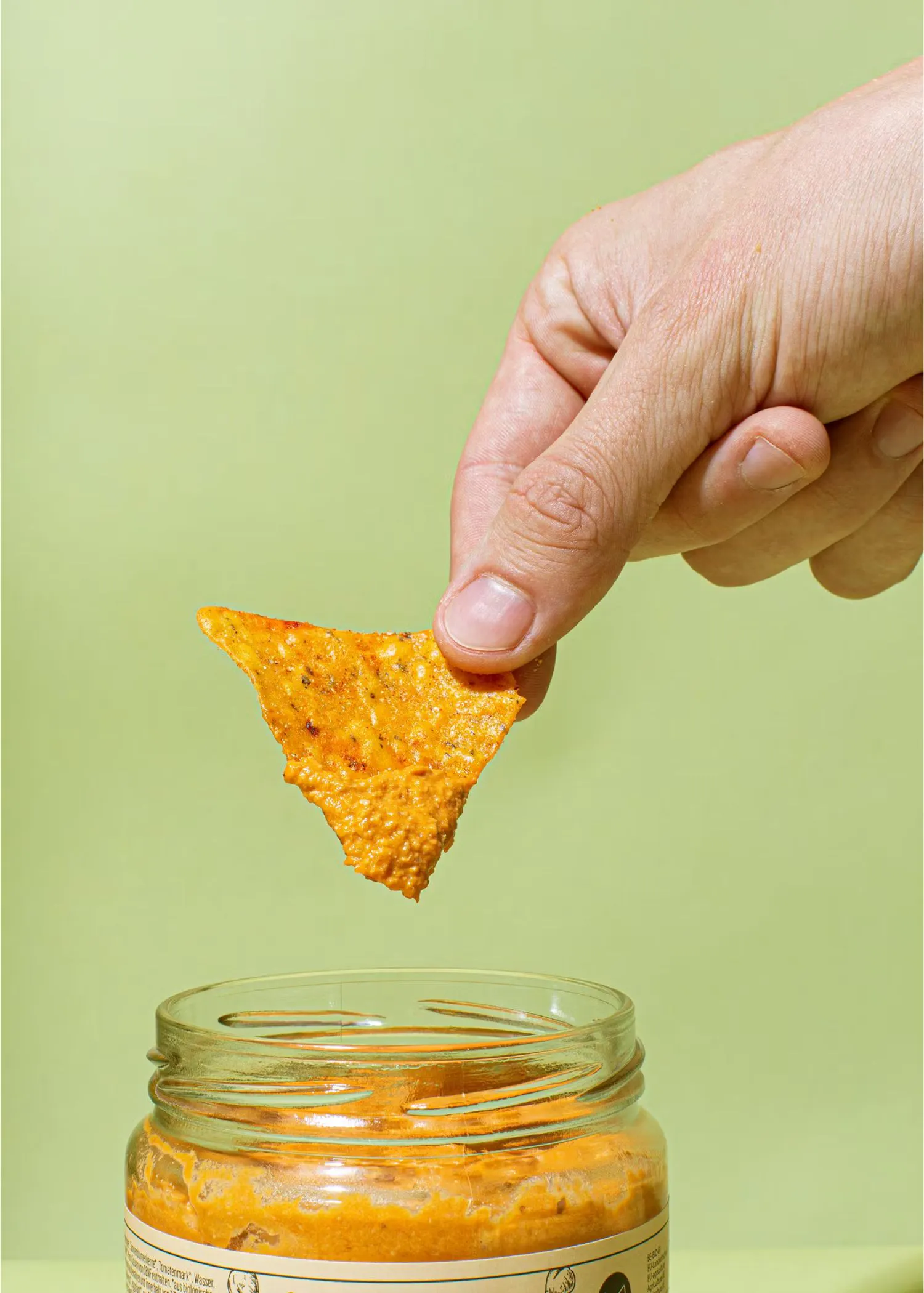 a hand dipping a tortilla chip into a jar of sauce