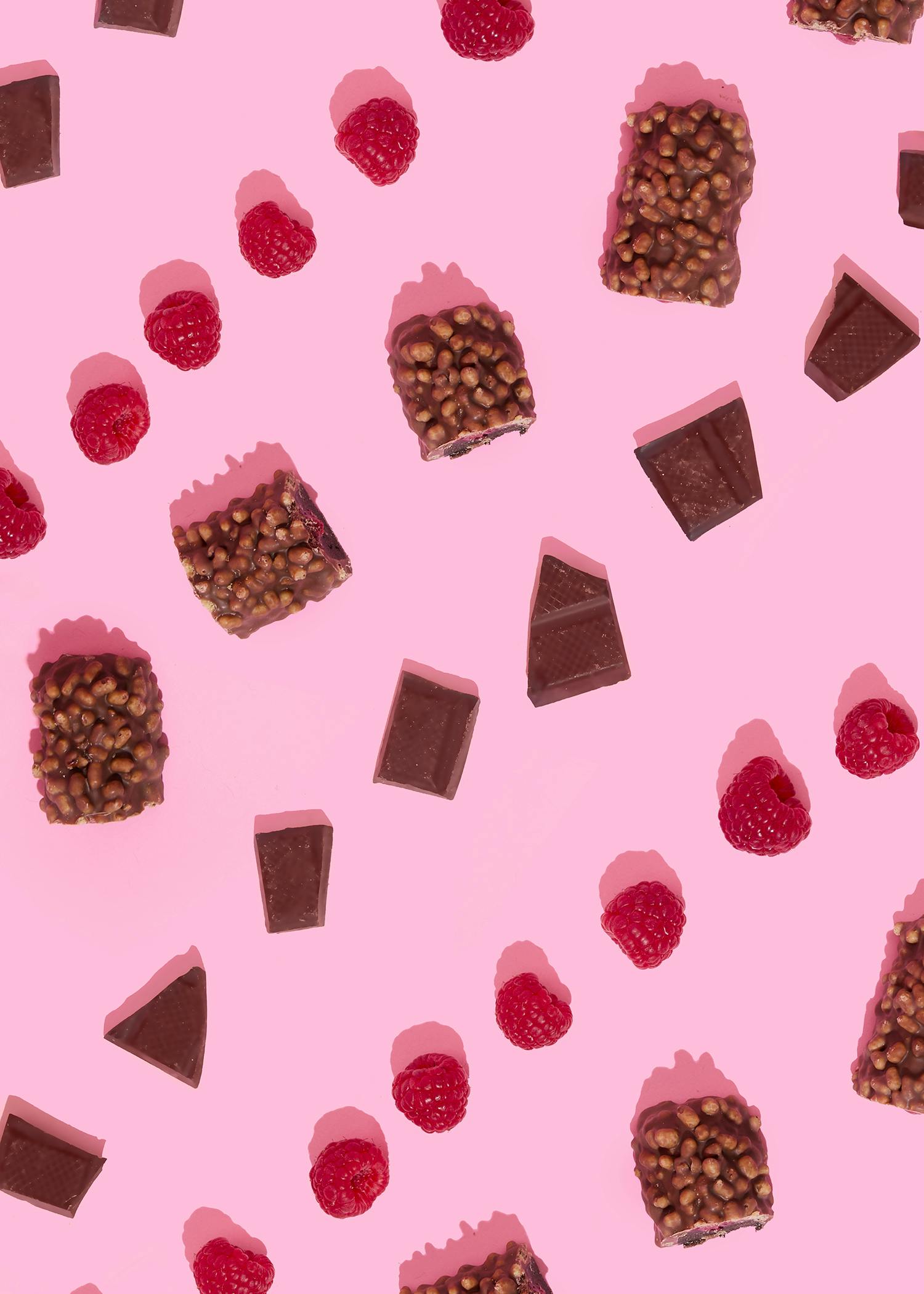 pieces of chocolate and raspberries on a pink background